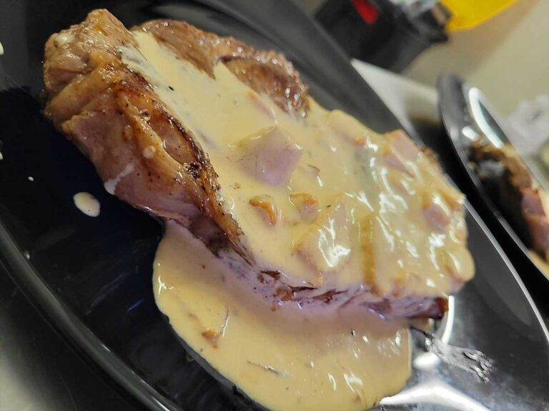 Une entrecôte juteuse et parfaitement saisie, nappée d'une sauce onctueuse aux éclats de cèpes, servie avec élégance sur une assiette sombre au restaurant du Château le Verdoyer.