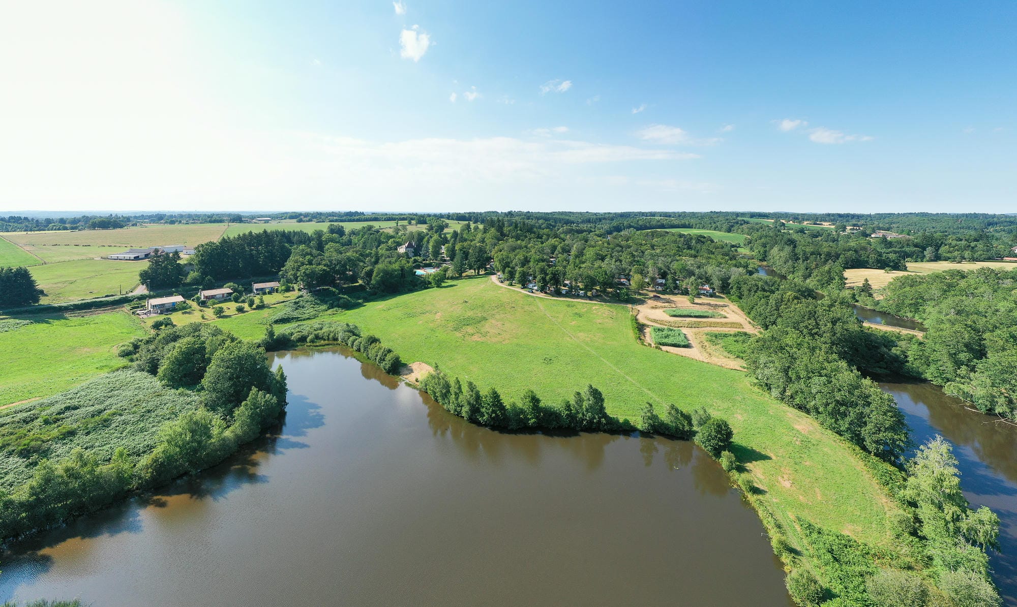 Vue aérienne de l'étang de baignade du Camping Château le Verdoyer et de sa plage dans un cadre verdoyant