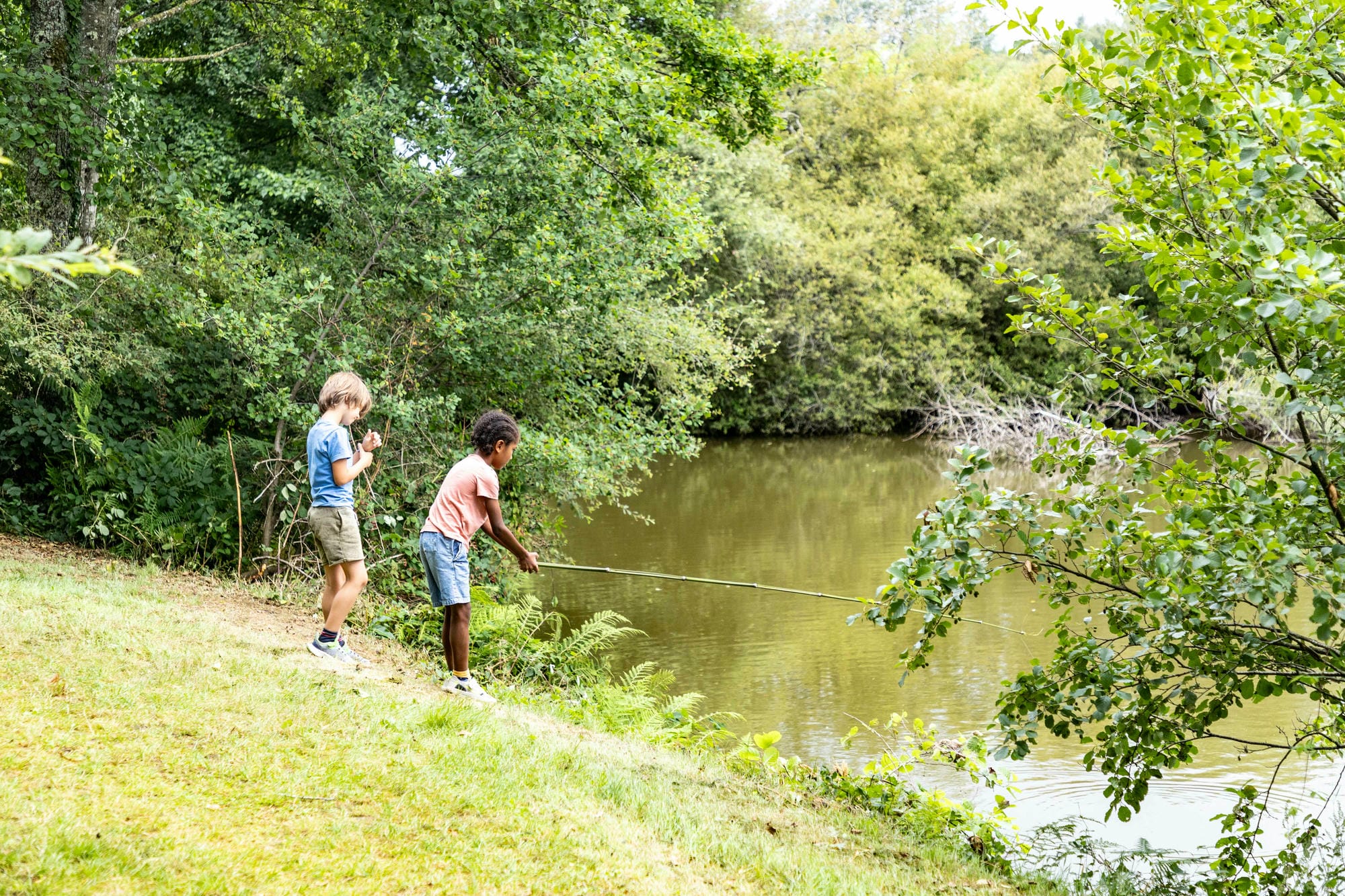 Deux garçons pêchant sur la rive boisée de l'étang du Camping Château le Verdoyer