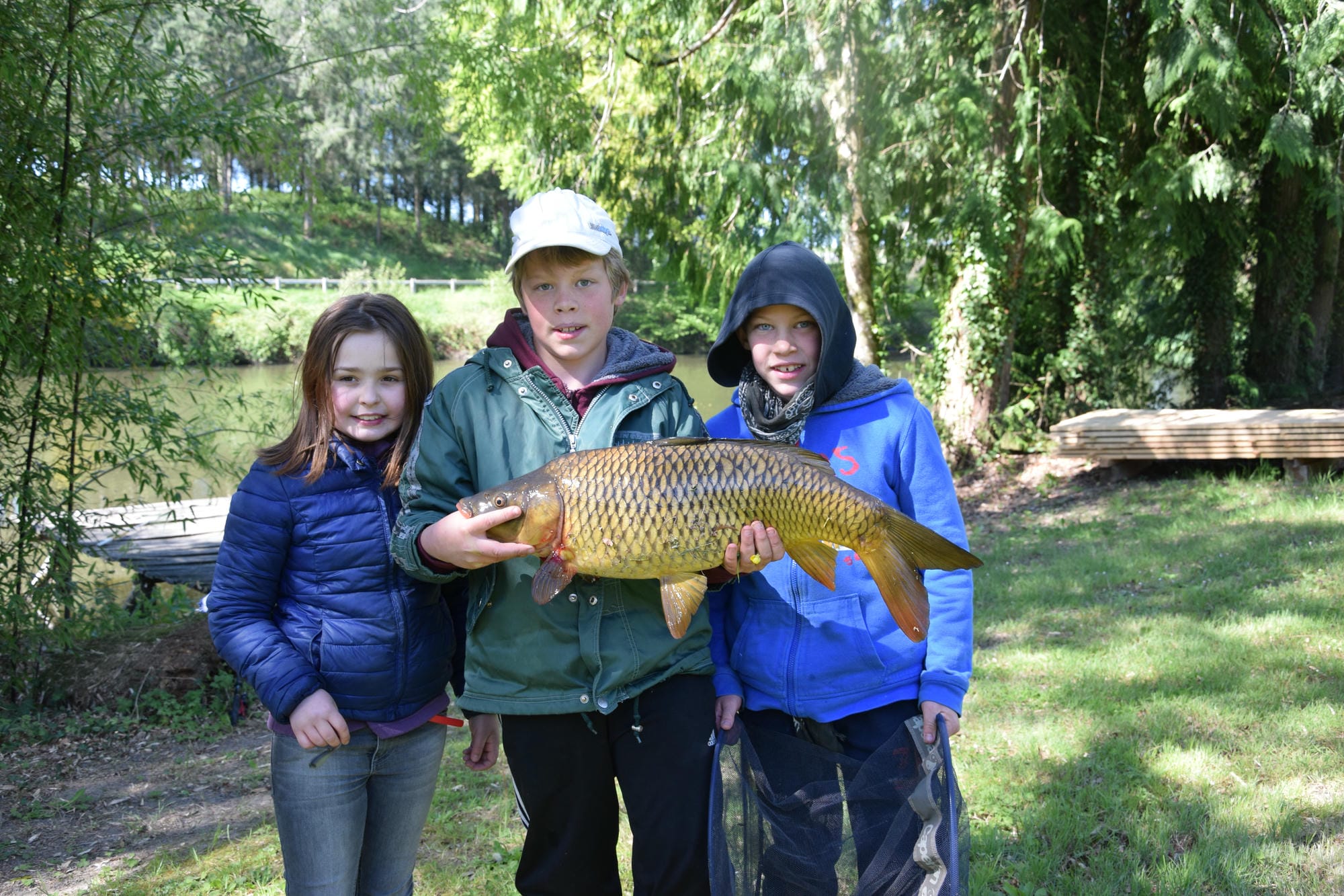 Trois enfants montrant fièrement un poisson pêché à l'étang du Verdoyer