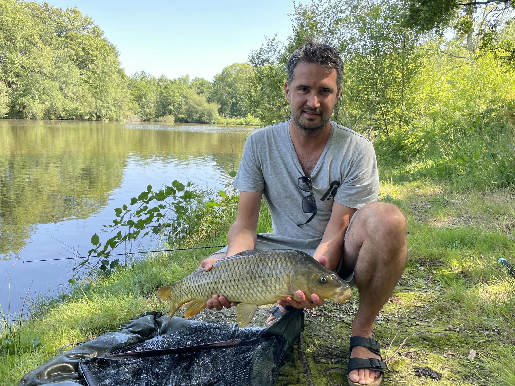 Homme agenouillé montrant fièrement sa prise, pêche à l'étang du Camping Château Le Verdoyer