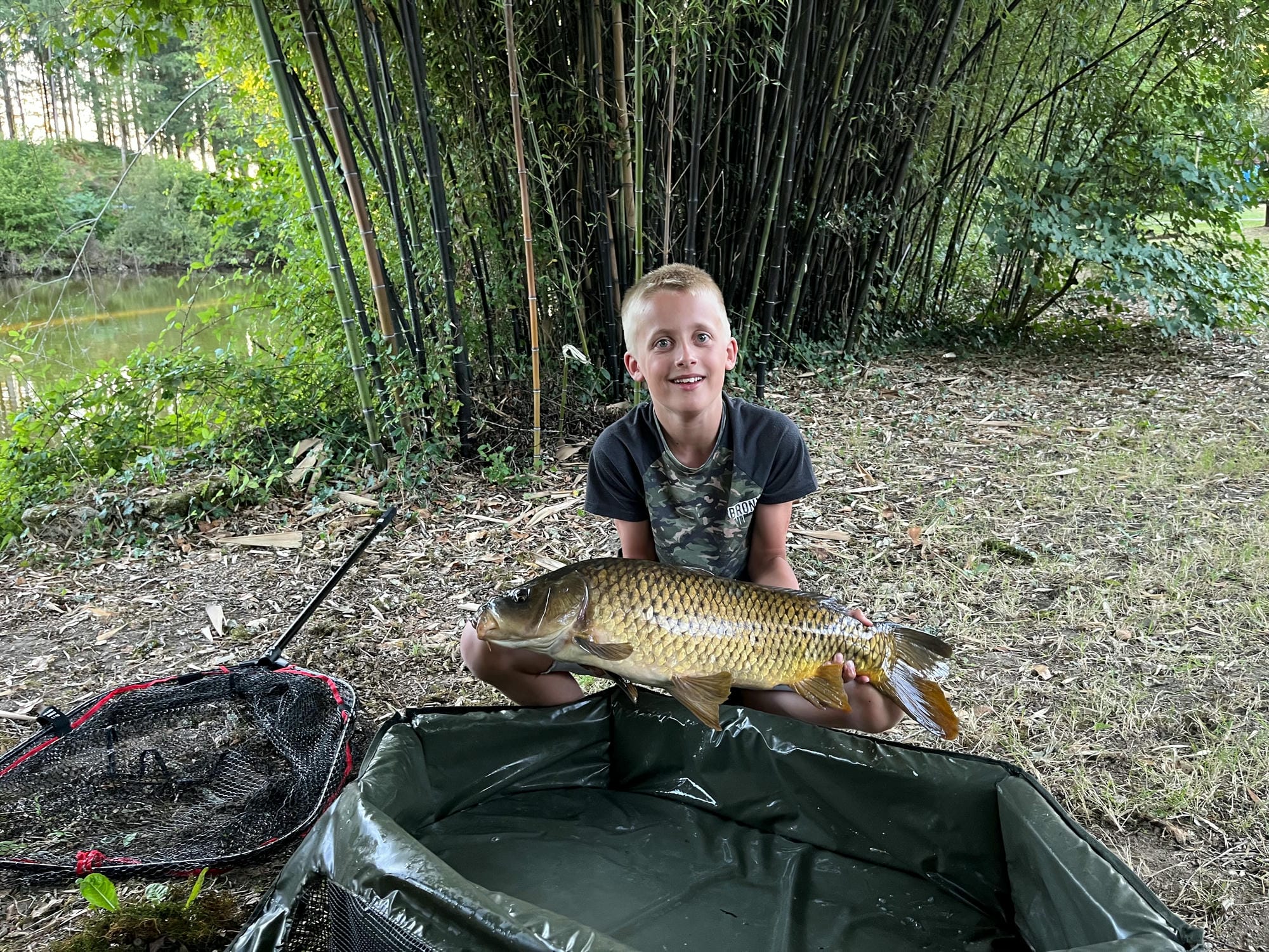 Garçon agenouillé tenant un poisson pêché dans l'étang du Camping Château le Verdoyer