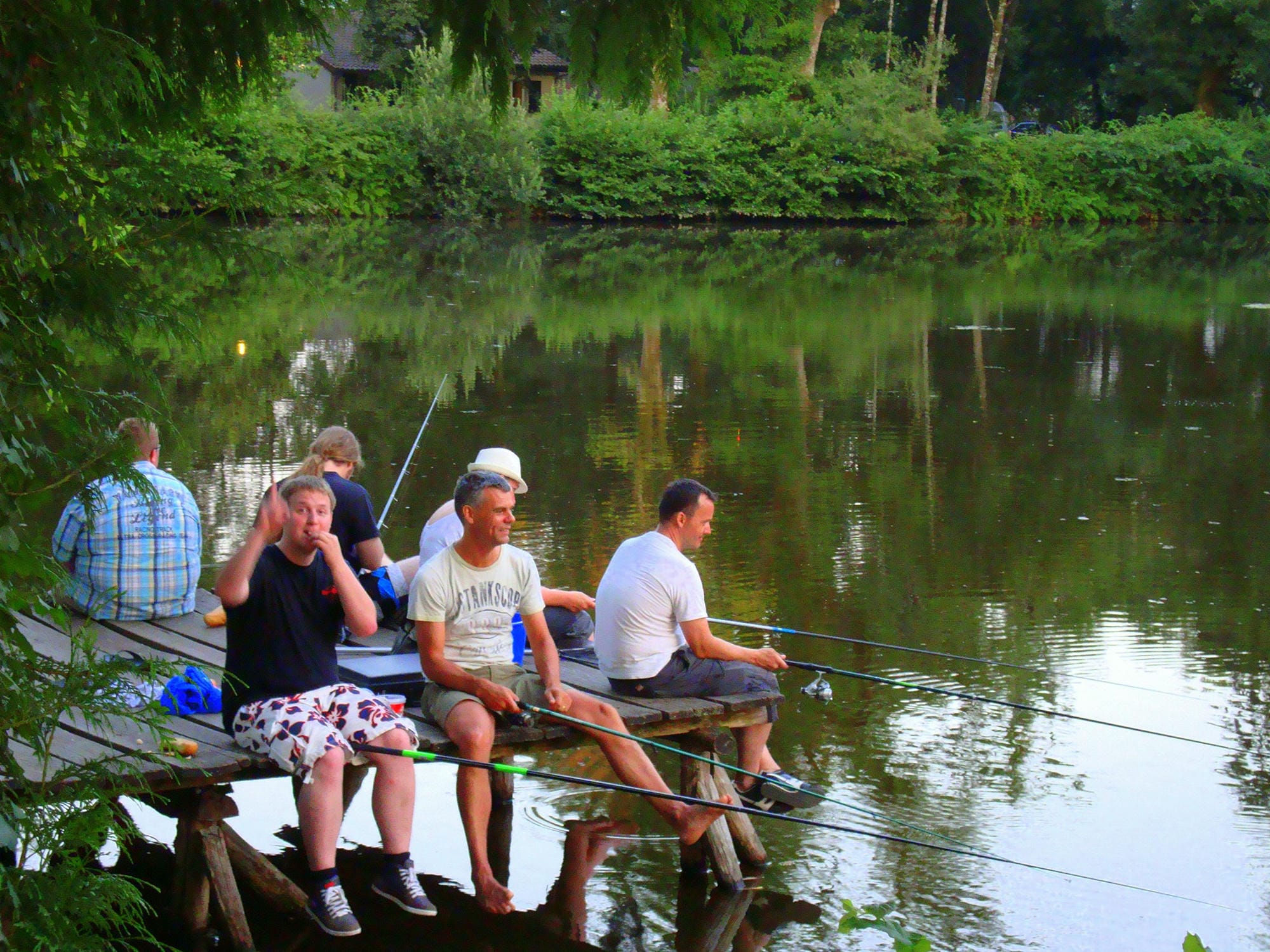 Plusieurs personnes assises sur un ponton pêchant à l'étang du Camping Château le Verdoyer