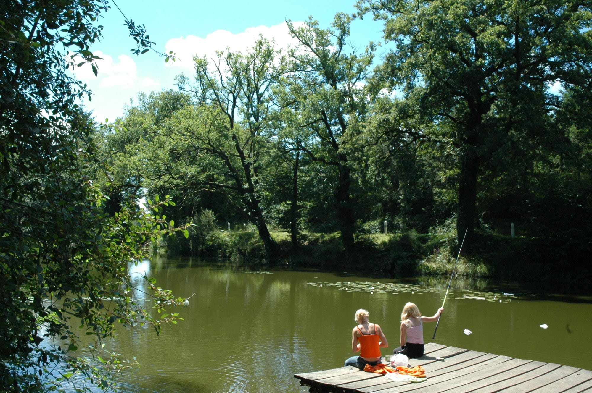 Deux enfants assis sur un ponton au bord de l'étang de pêche du Camping Le Verdoyer