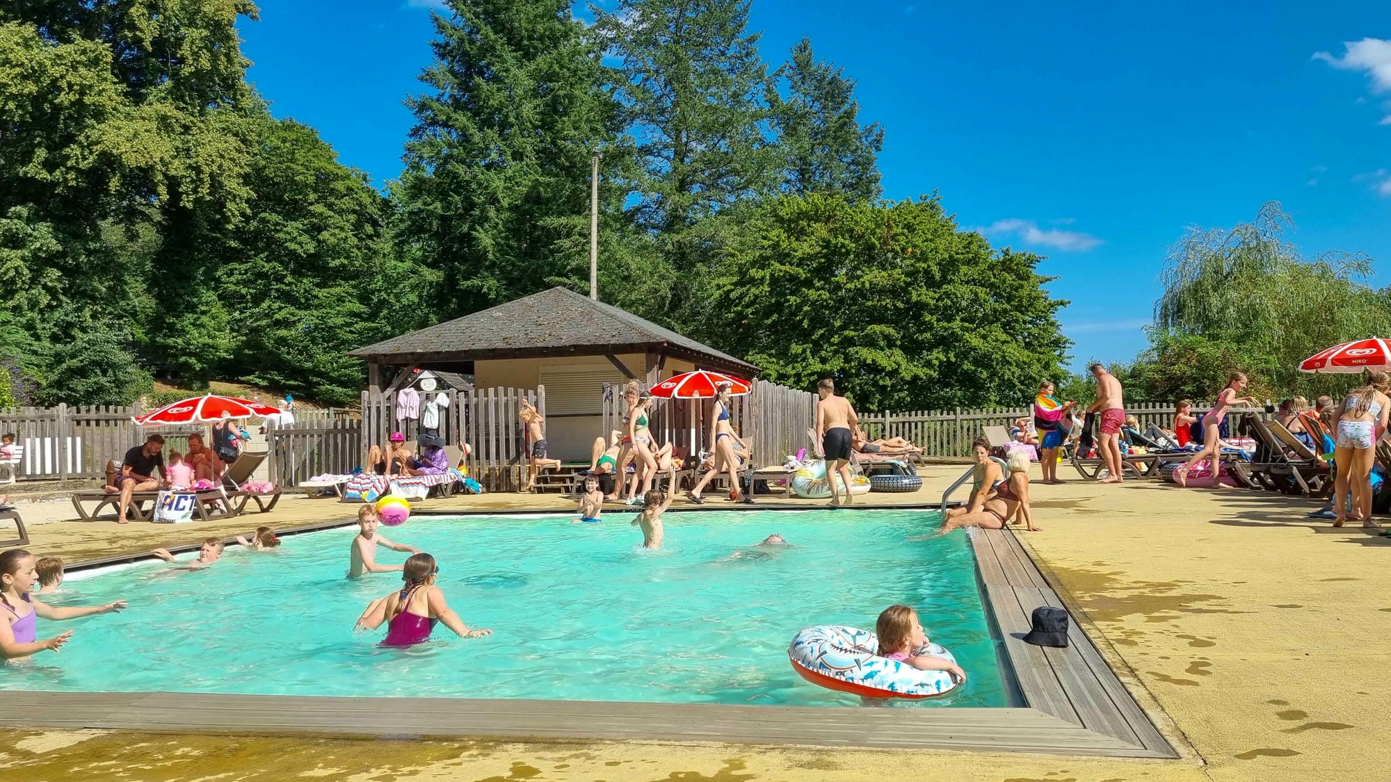 Vacanciers se relaxant à la piscine avec parasols au Camping Château le Verdoyer