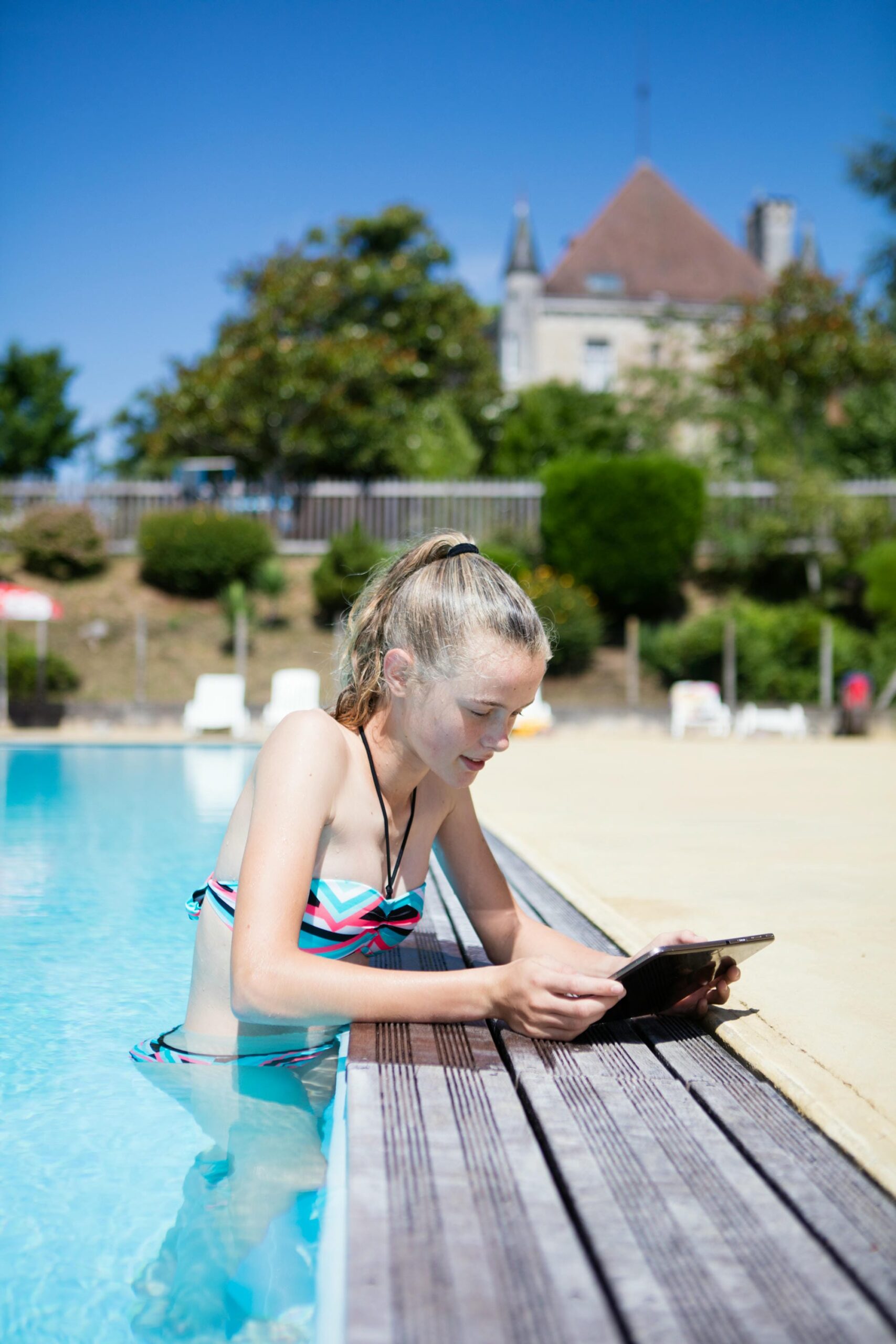 Femme blonde en bikini utilisant une tablette au bord de la piscine du Château le Verdoyer