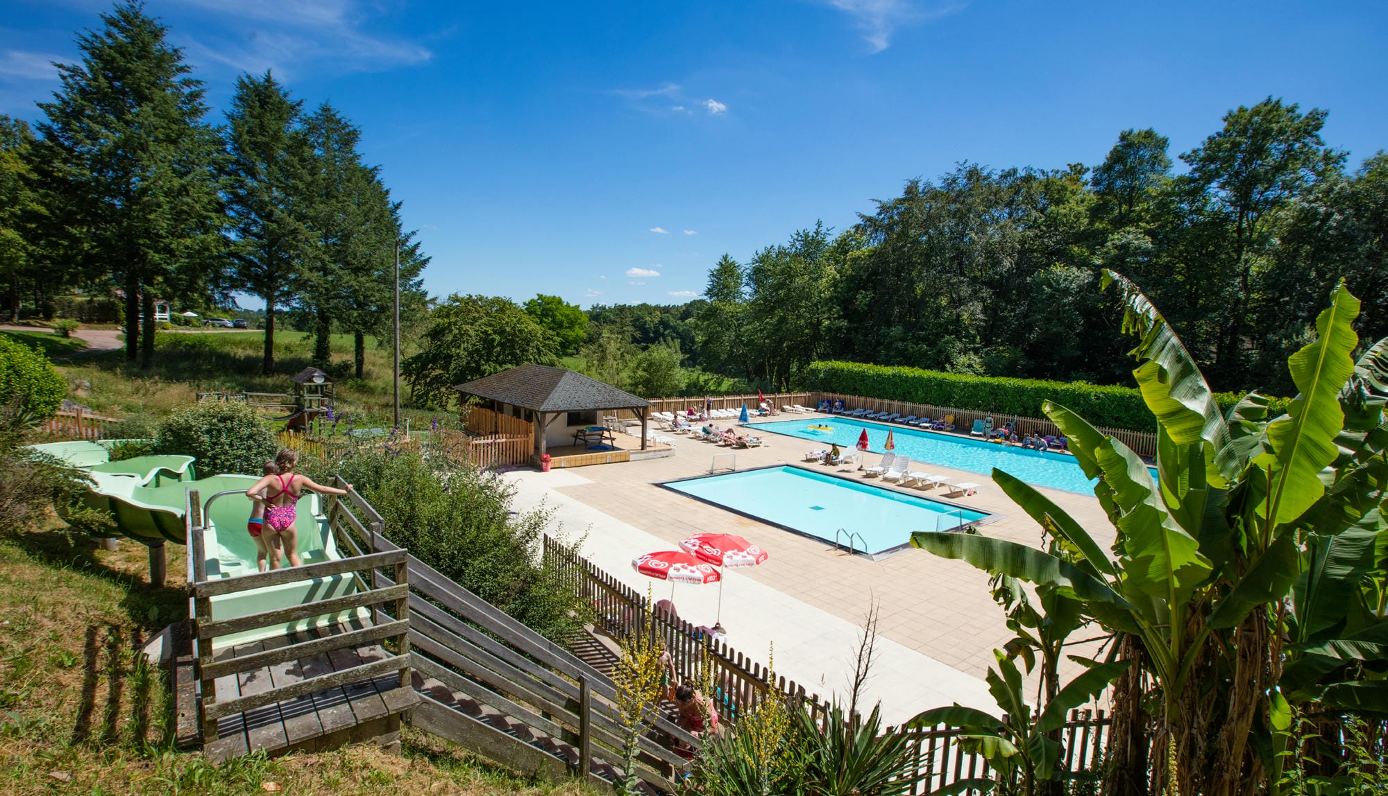 Piscine extérieure avec toboggan aquatique et pool house en arrière-plan au Camping Le Verdoyer