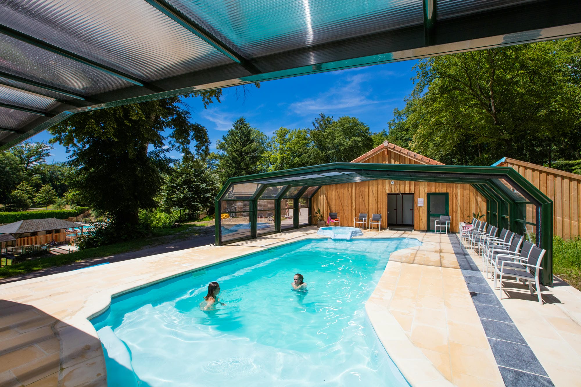 Couple nageant dans la piscine couverte avec jacuzzi, espace bien-être au Château le Verdoyer