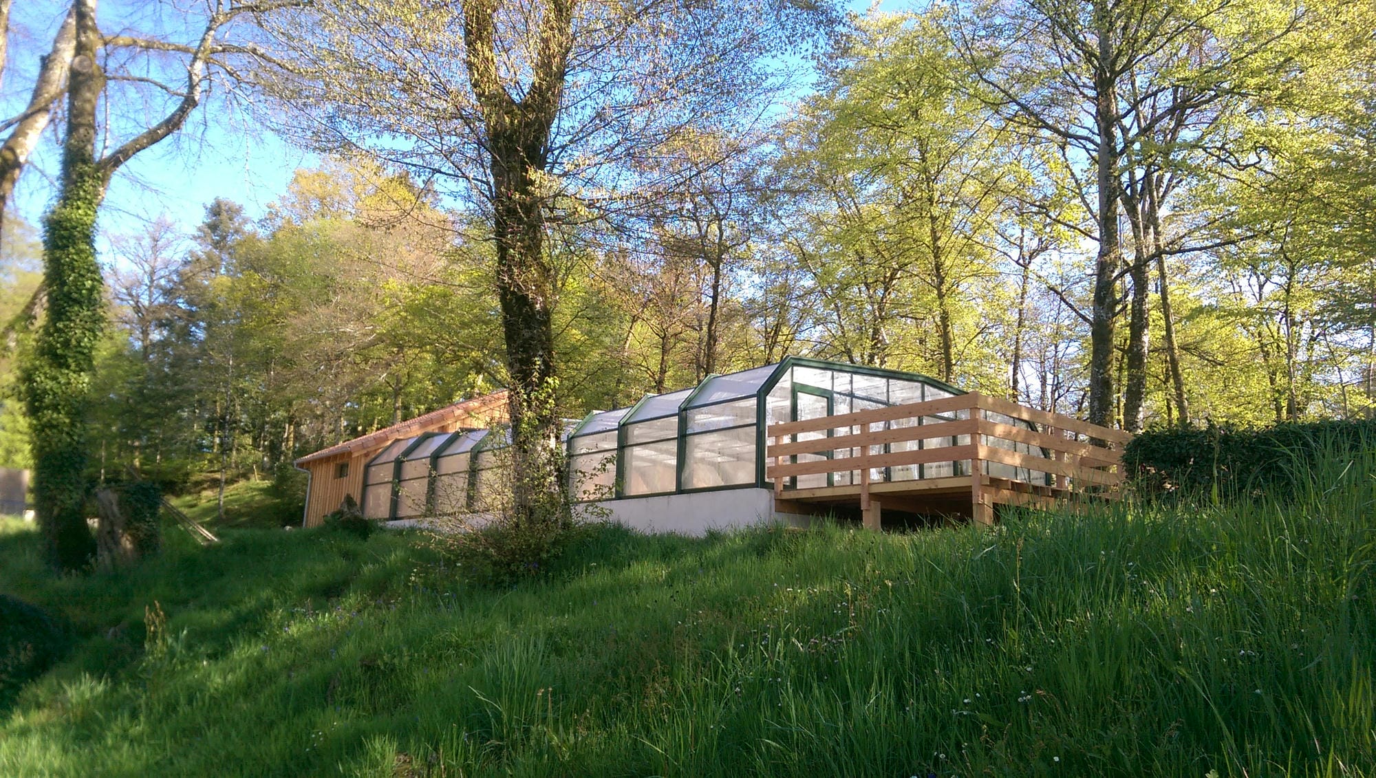 Vue extérieure de la piscine couverte et jacuzzi, bâtiment niché dans la verdure du Camping Le Verdoyer