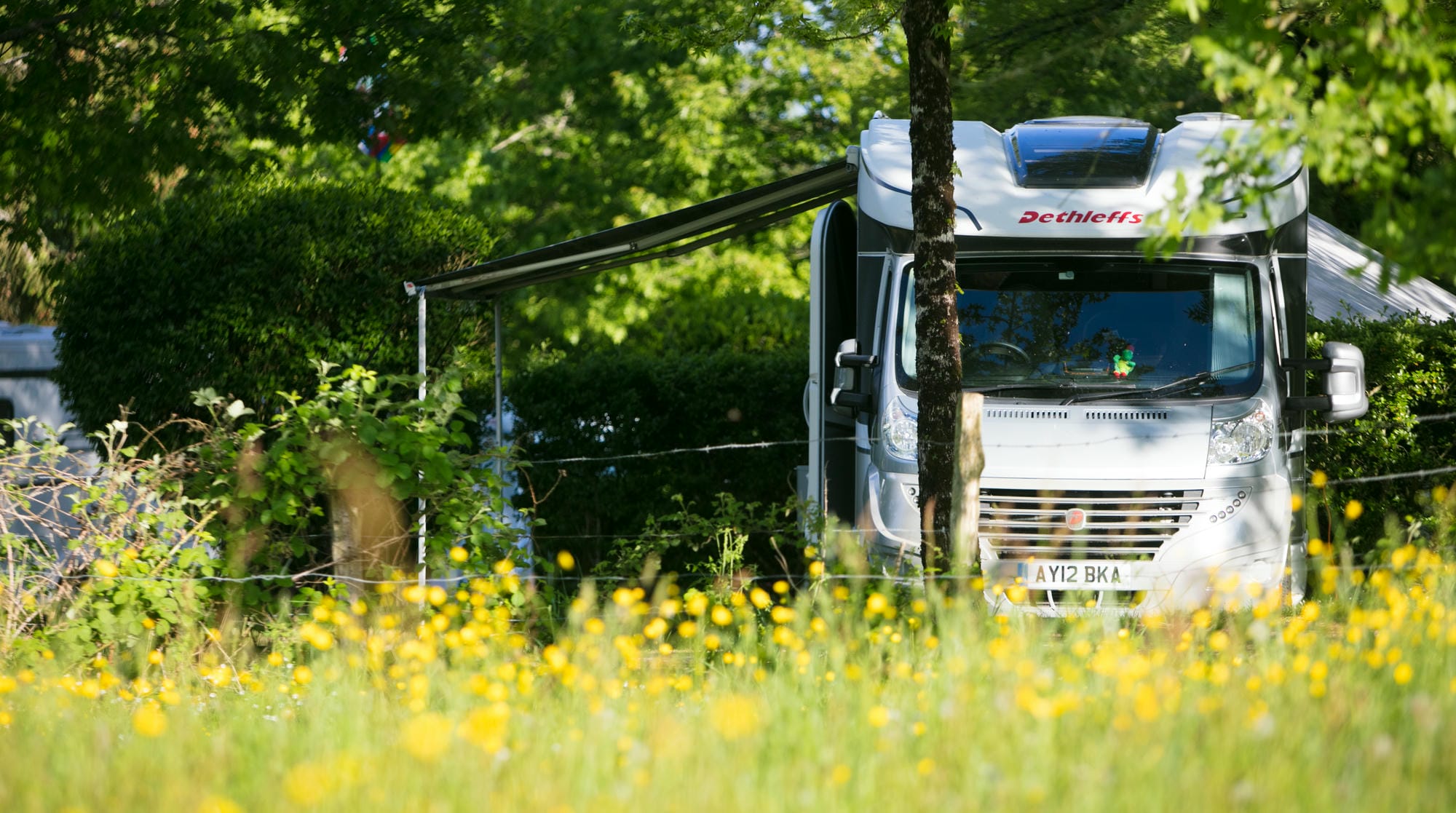 Camping Car Dethleffs blanc garé dans un champ de fleurs jaunes, emplacement nature au Camping Le Verdoyer