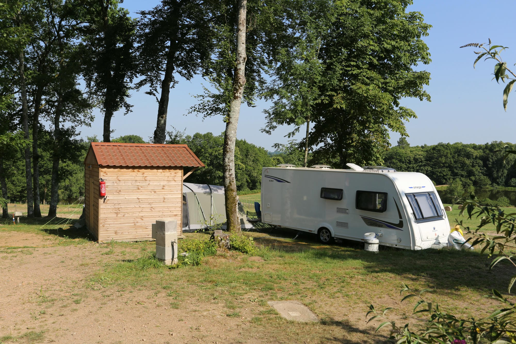 Caravane blanche garée à côté d'un sanitaire individuel en bois, camping au Verdoyer