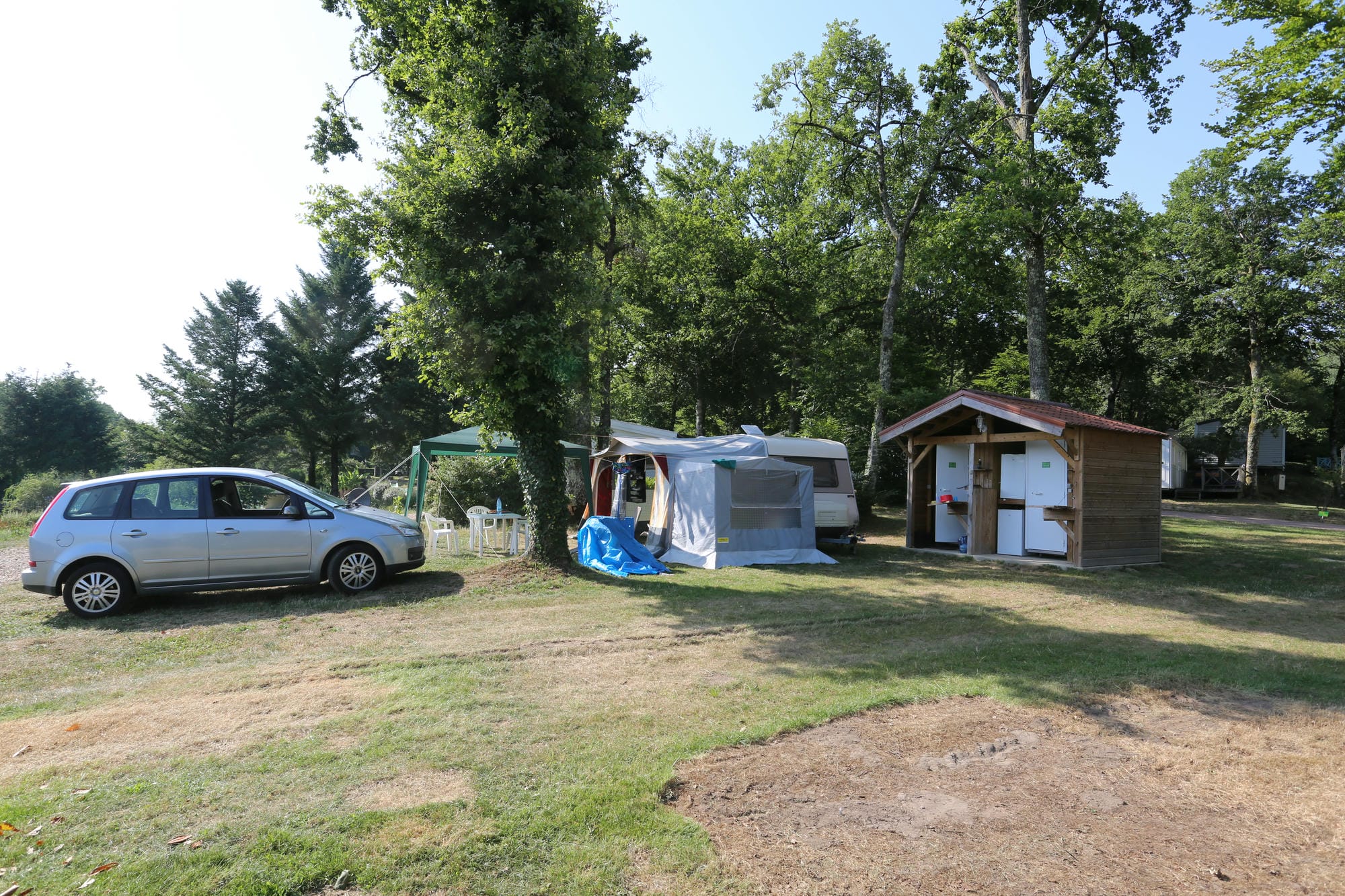 Voiture garée à côté d'une petite tente sur un emplacement herbeux au Camping Le Verdoyer
