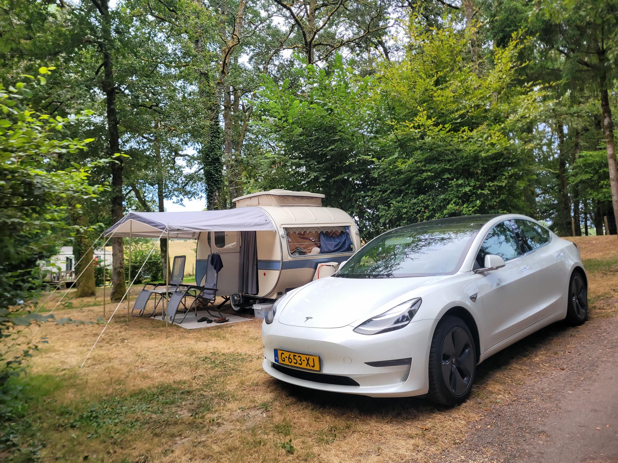 Voiture moderne garée à côté d'une caravane rétro sur un emplacement boisé au Camping Château le Verdoyer