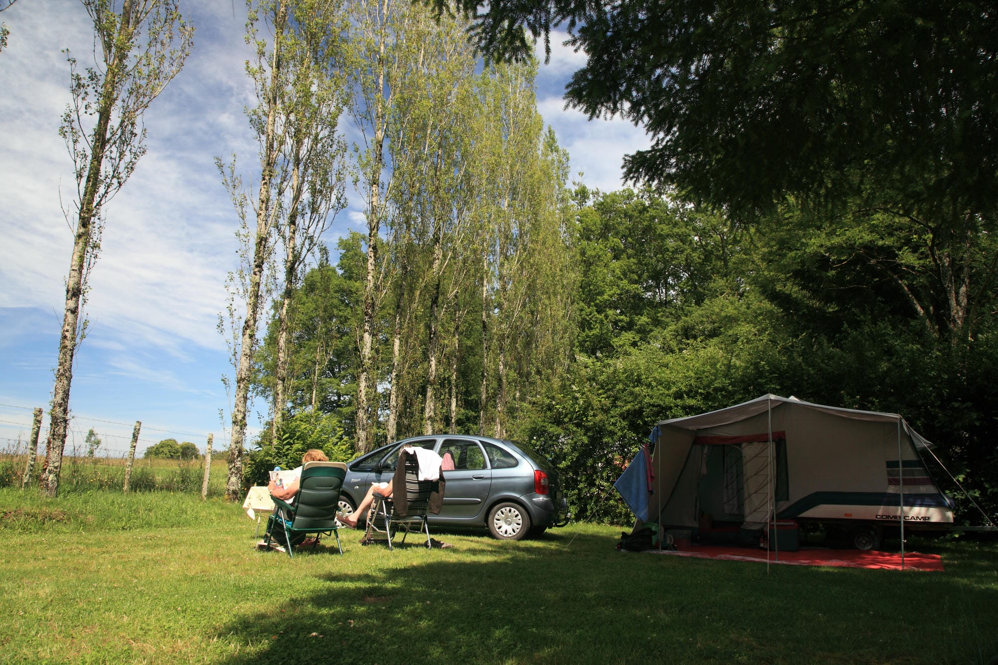 Voiture garée dans l'herbe à côté d'une tente, emplacement de camping au Château le Verdoyer