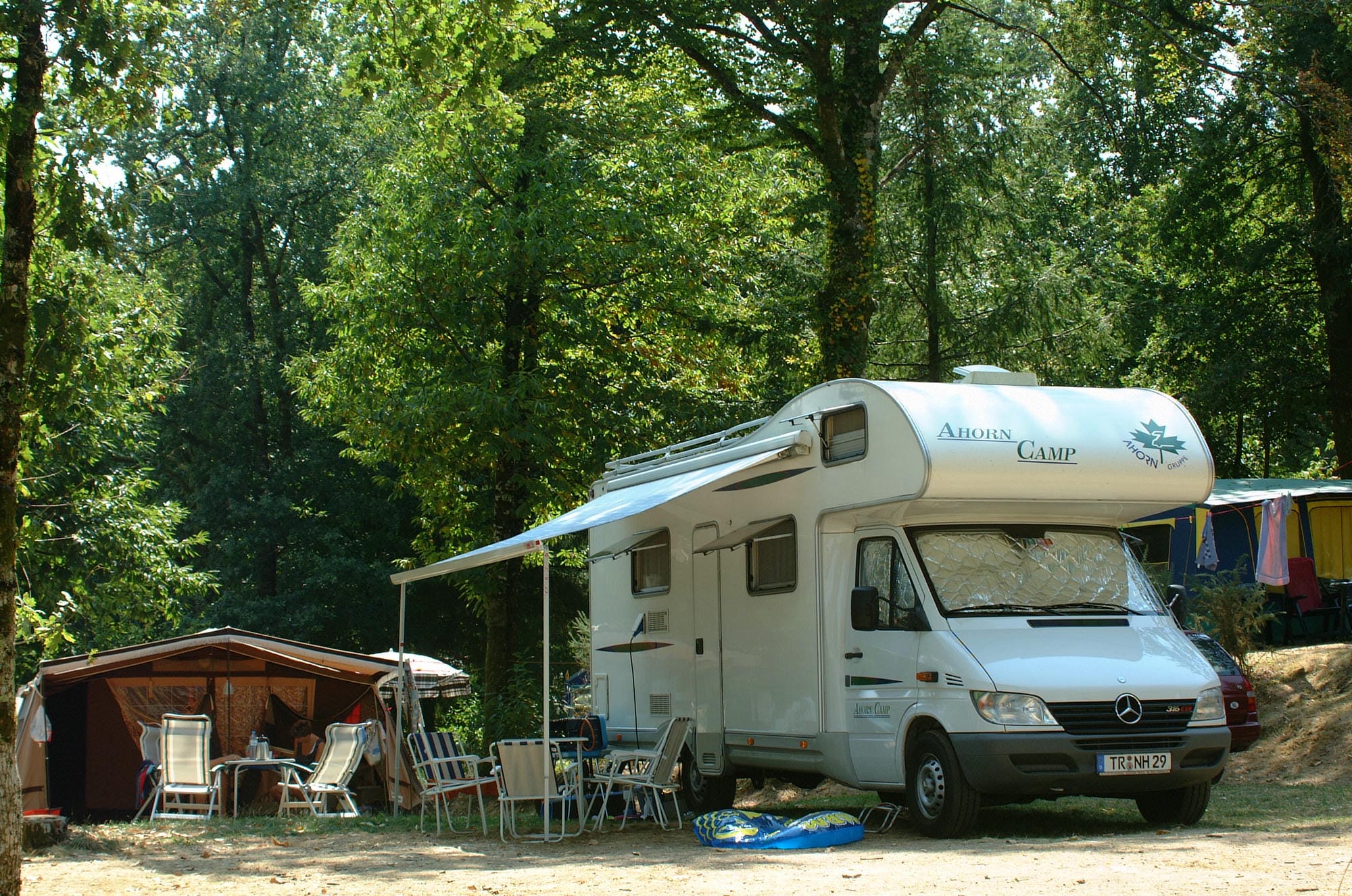 Camping car garé sur un emplacement boisé avec une tente, camping nature au Château le Verdoyer
