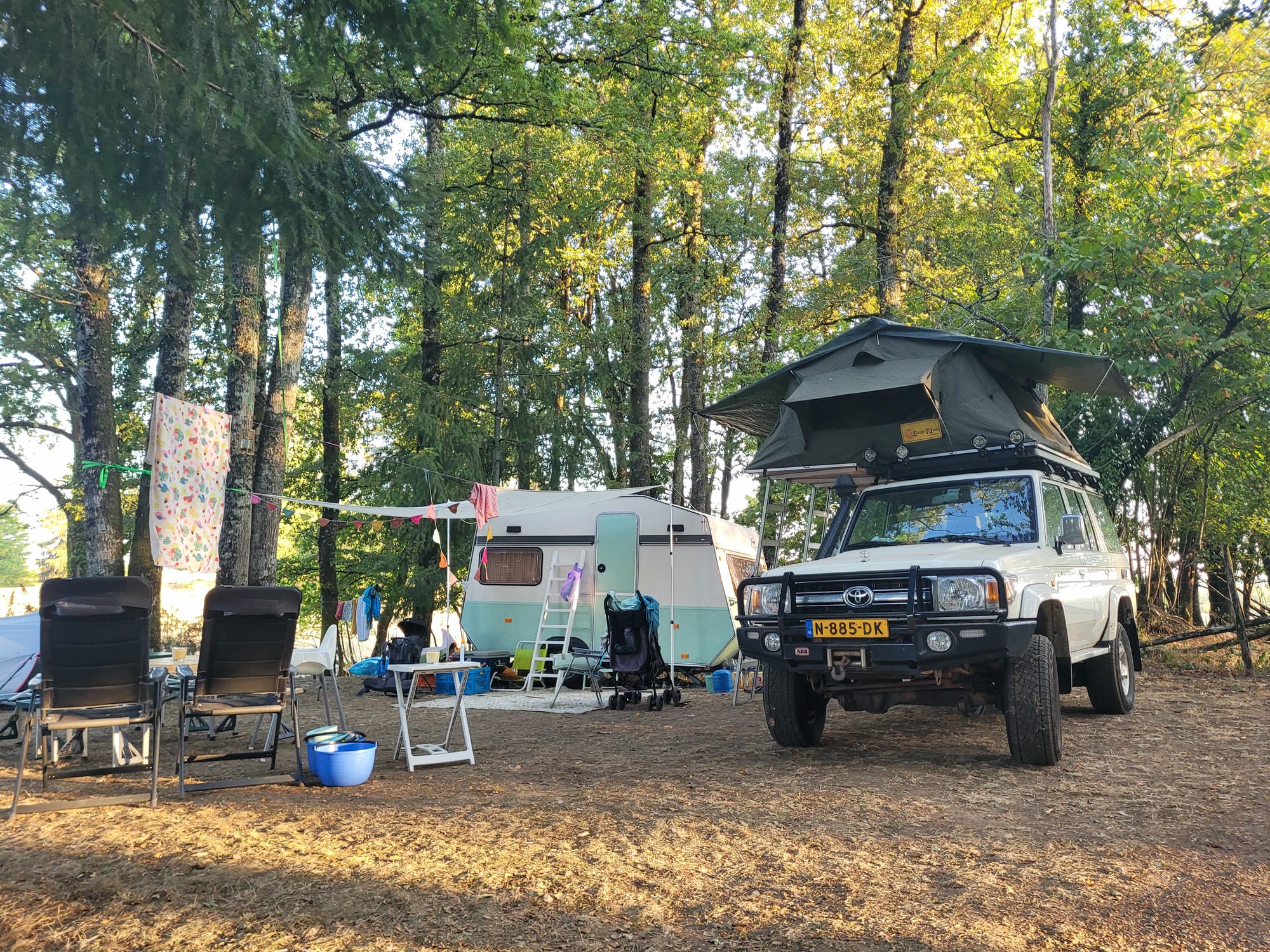 Pick-up avec cellule et remorque-tente sur un emplacement boisé au Camping Le Verdoyer