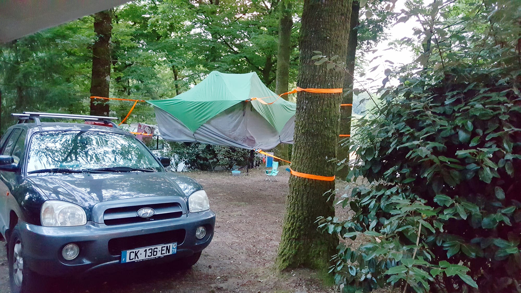 Voiture et tente suspendue sur un emplacement boisé au Camping Le Verdoyer