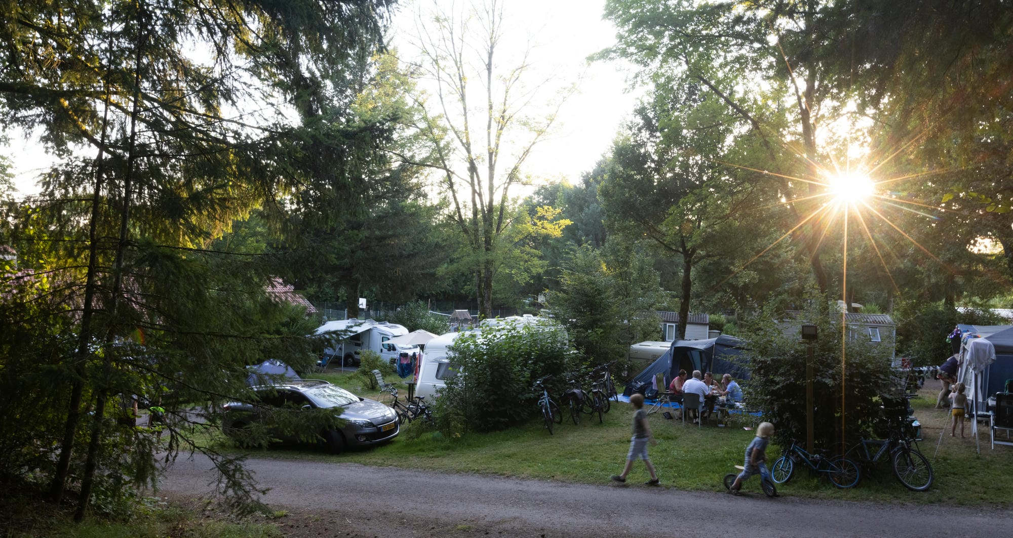 Nombreuses tentes et vélos sur des emplacements de camping herbeux près d'une allée au Verdoyer