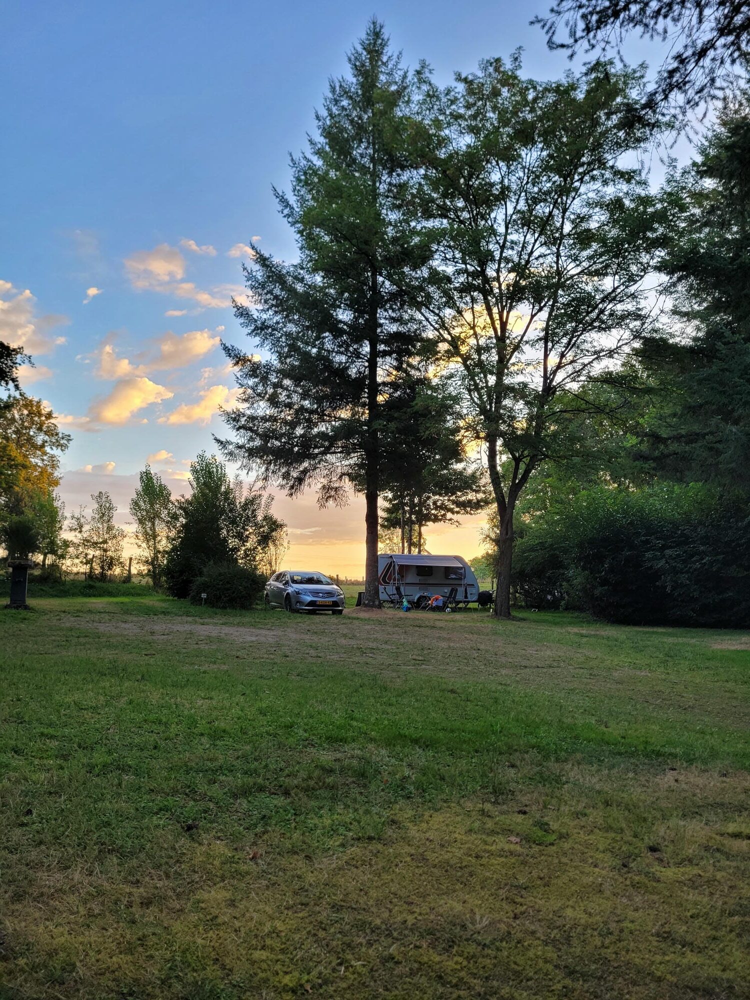 Une caravane sur un emplacement de camping arboré au Château le Verdoyer au couché du soleil