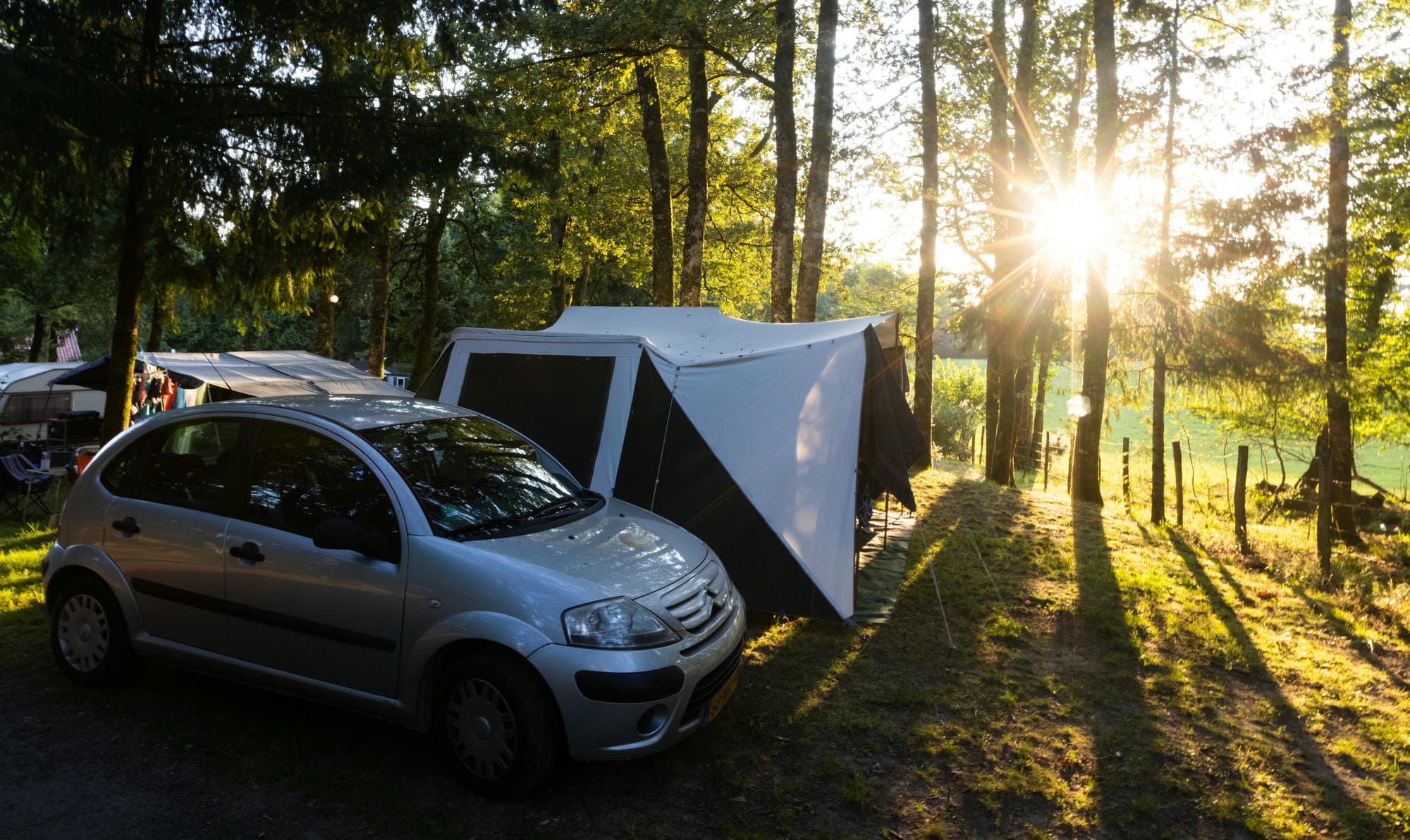 Voiture avec tente sur un emplacement de camping en forêt au Château le Verdoyer