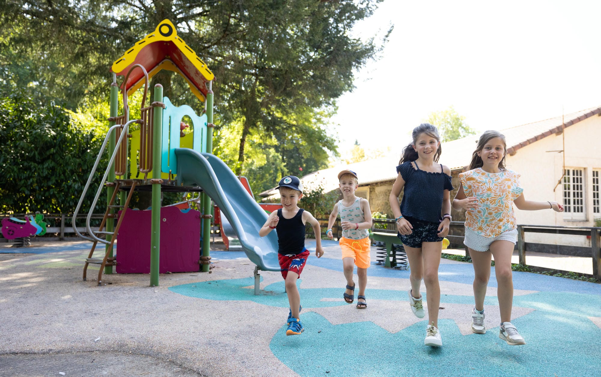 Enfants heureux courant sur l'aire de jeux sécurisée du camping familial Château le Verdoyer