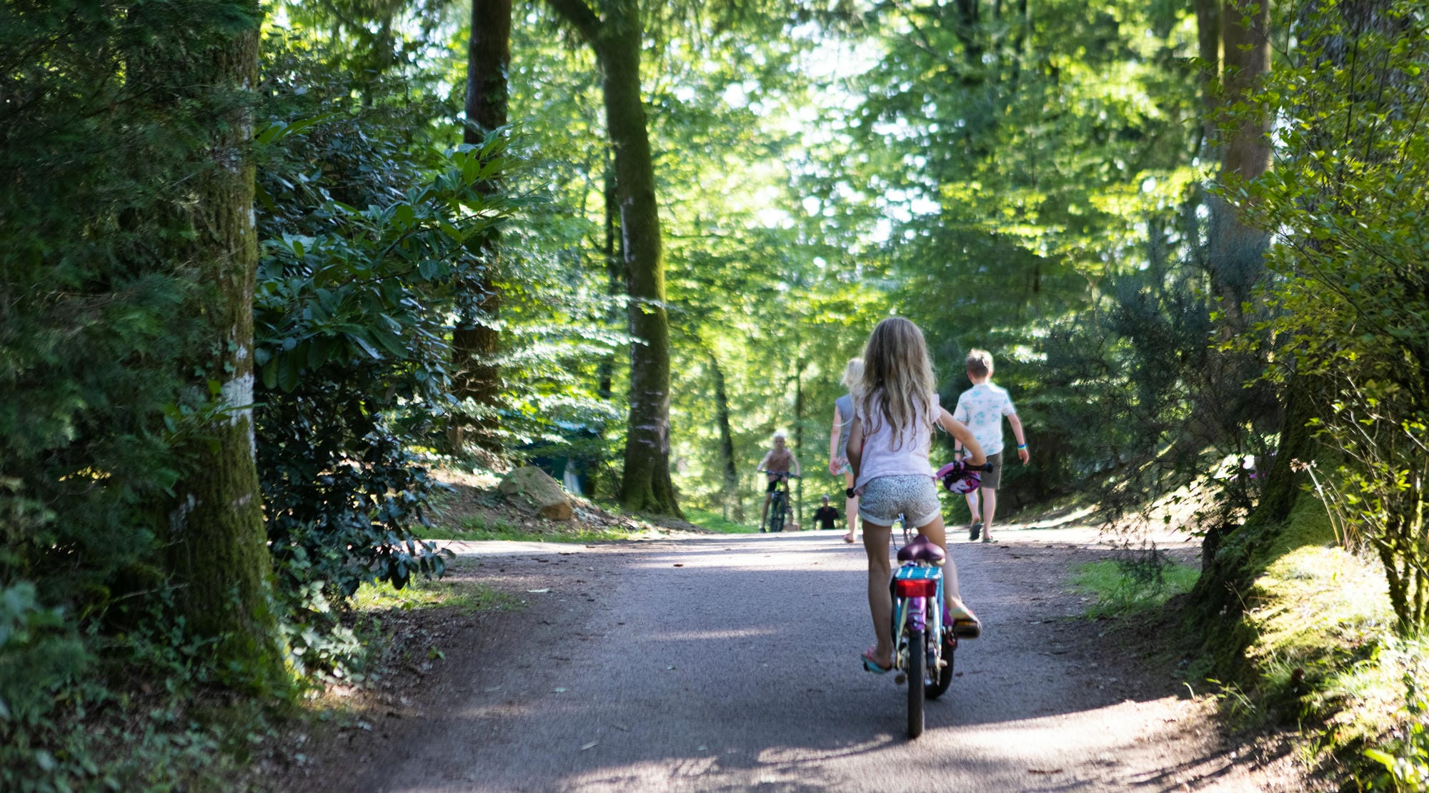 Enfant à vélo sur un sentier boisé, activité en famille au Camping Château Le Verdoyer