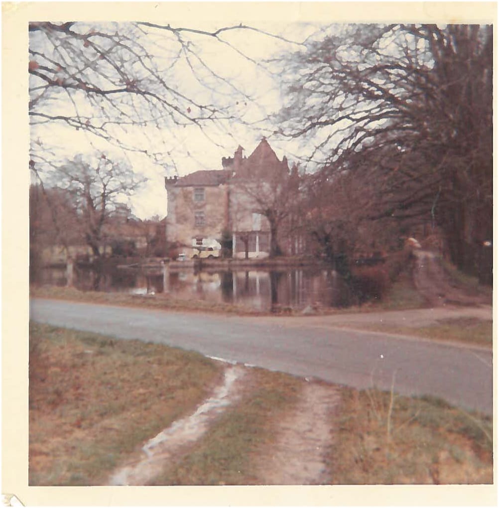 Photographie teintée du château vue depuis l'autre rive, plan d'eau, arbres nus en hiver, chemin d'accès