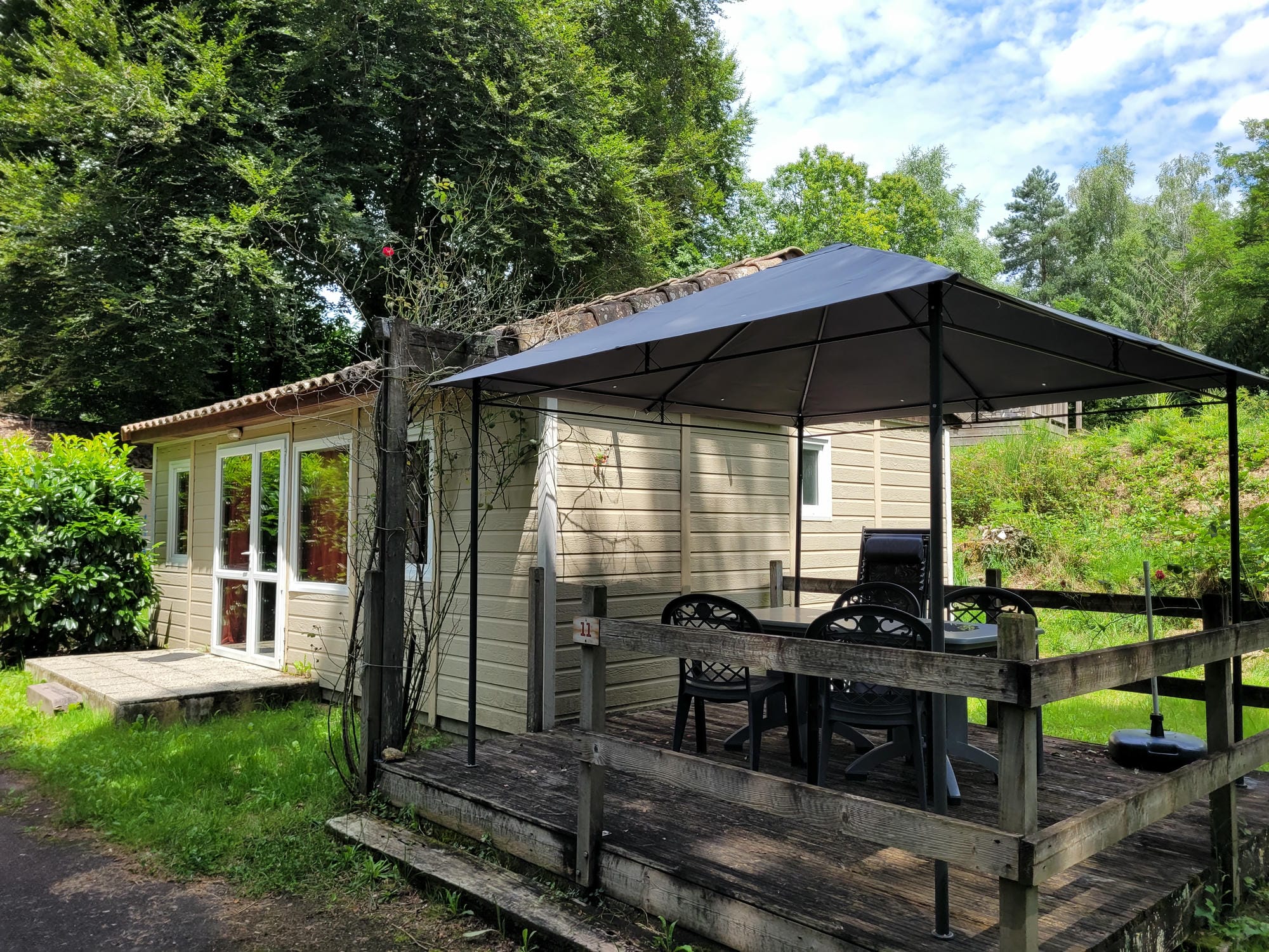 Chalet en bois avec terrasse couverte et table, hébergement de plein air au Camping Château le Verdoyer