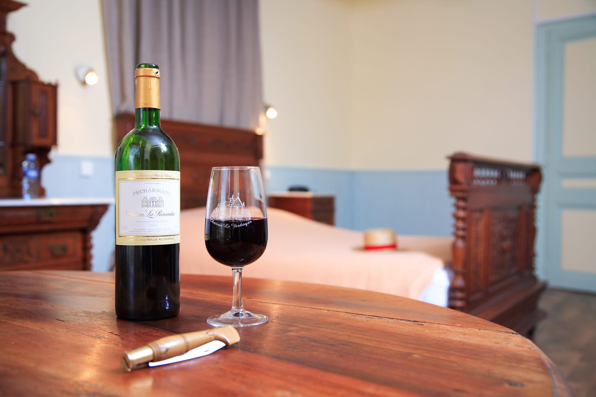 Bouteille de vin et verre sur une table dans la chambre 11 du Château le Verdoyer, accueil privilégié