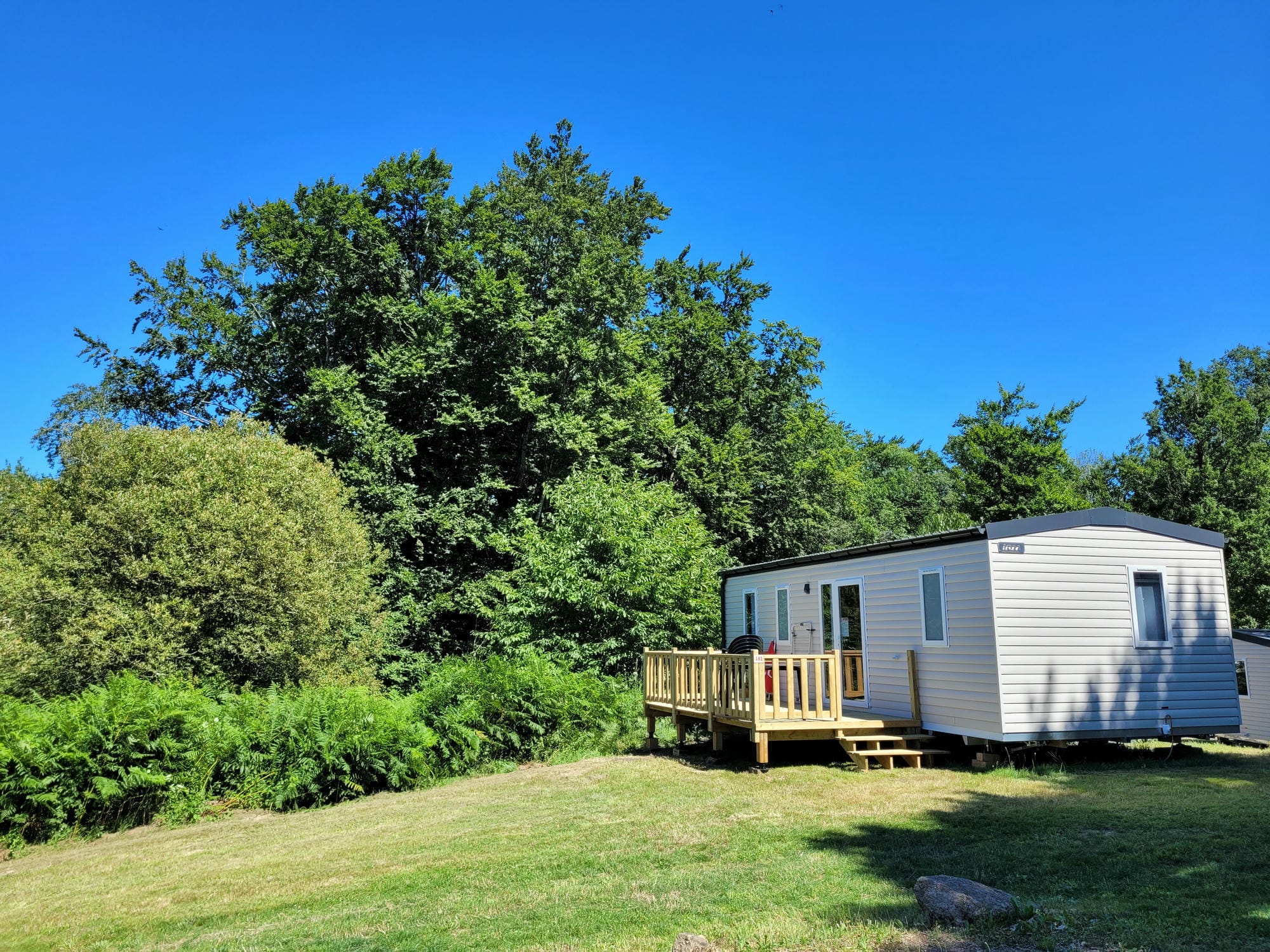 Mobil-home 3 chambres sur une petite terrasse en bois dans l'herbe, Camping Le Verdoyer
