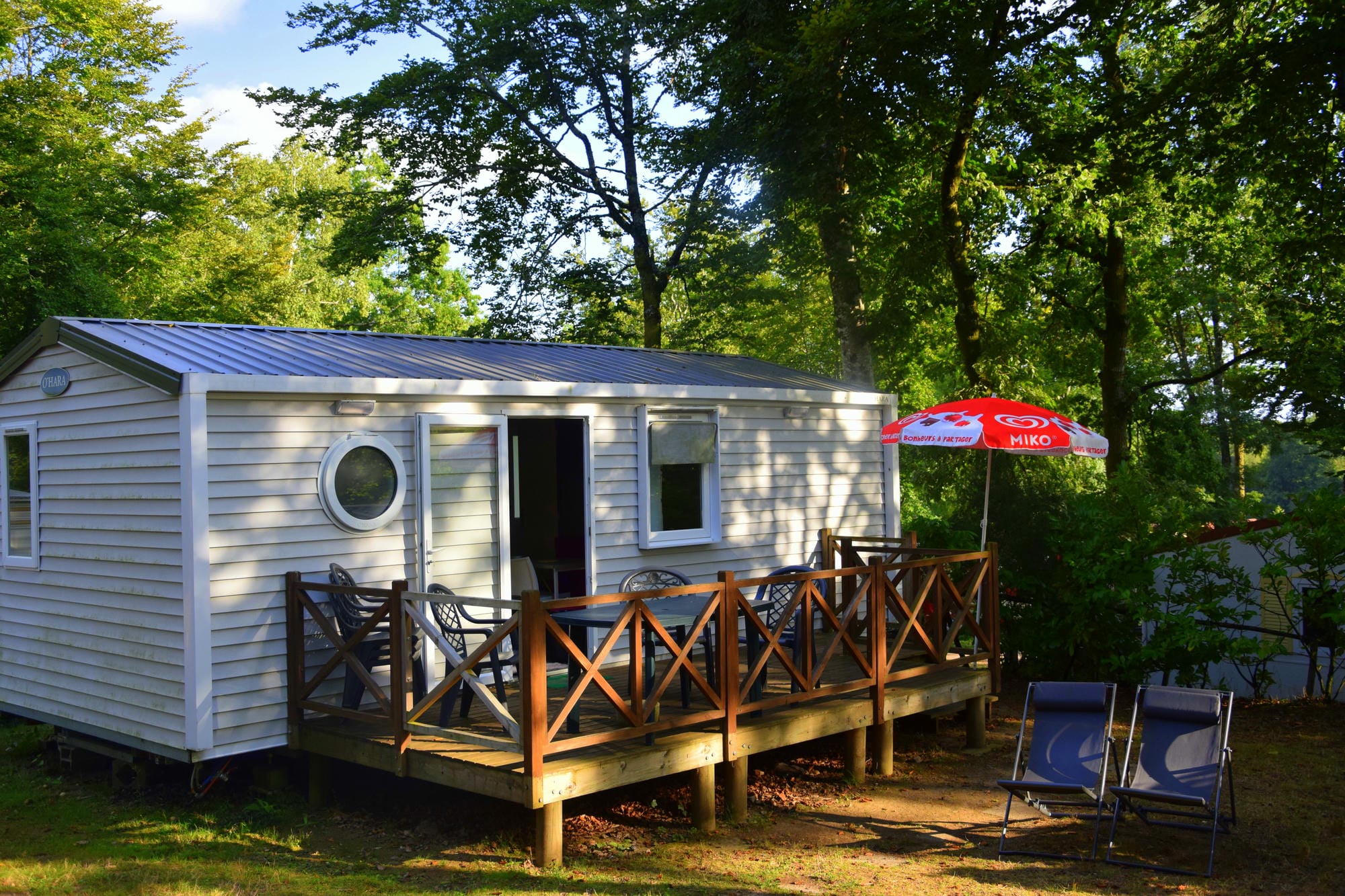Mobil-home de luxe blanc avec terrasse en bois et parasol rouge, hébergement haut de gamme au Verdoyer