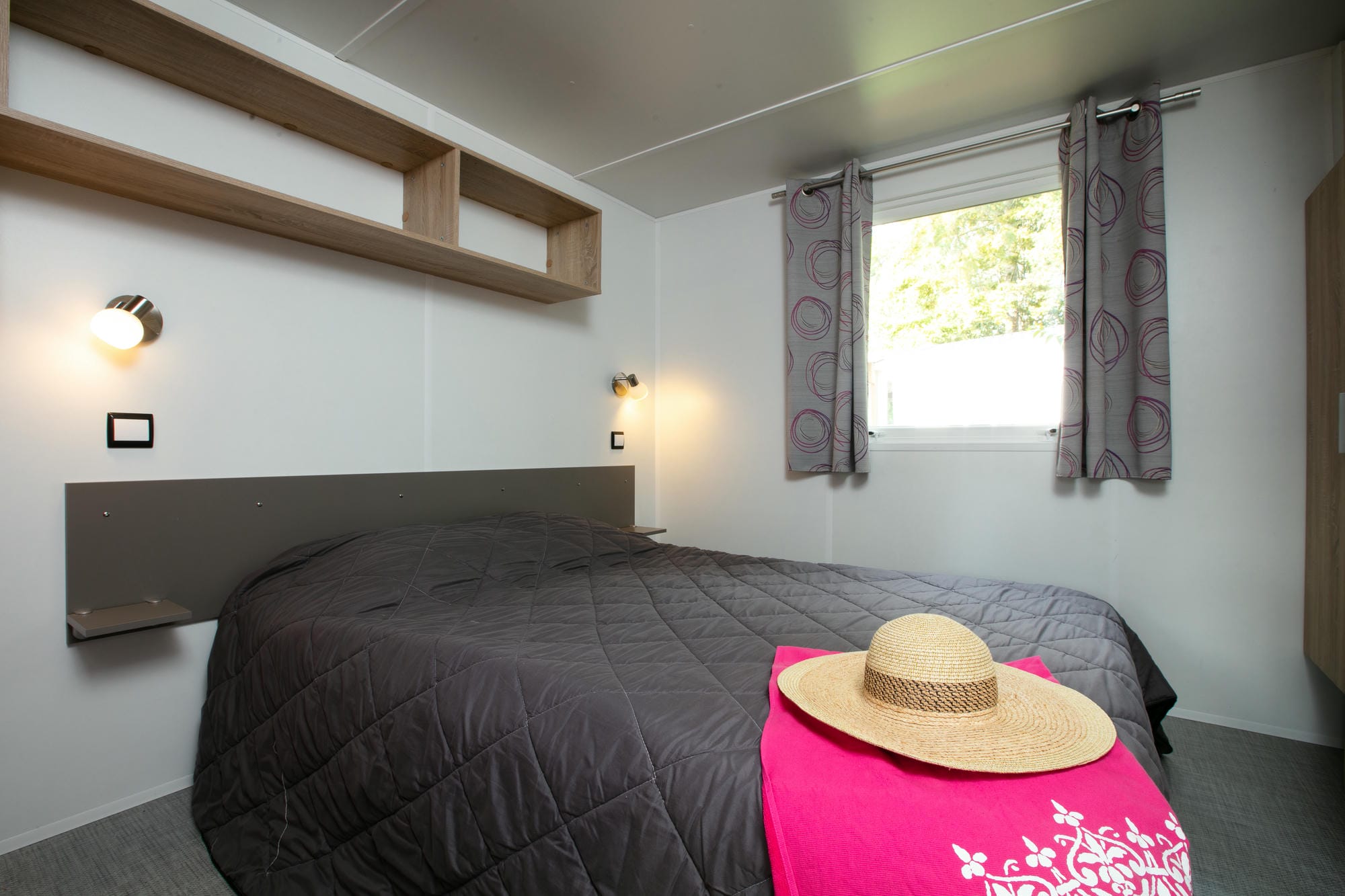 Lit avec un chapeau posé dessus dans un mobil-home de luxe, ambiance vacances au Verdoyer