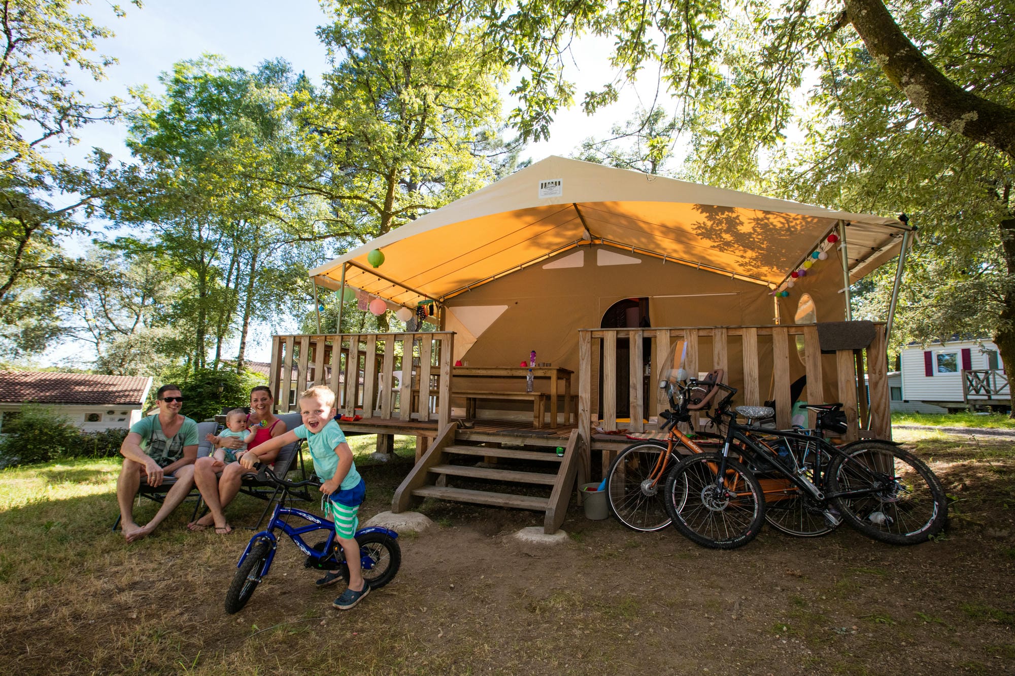 Vacanciers sous une tente lodge avec vélos, hébergement glamping au Château le Verdoyer