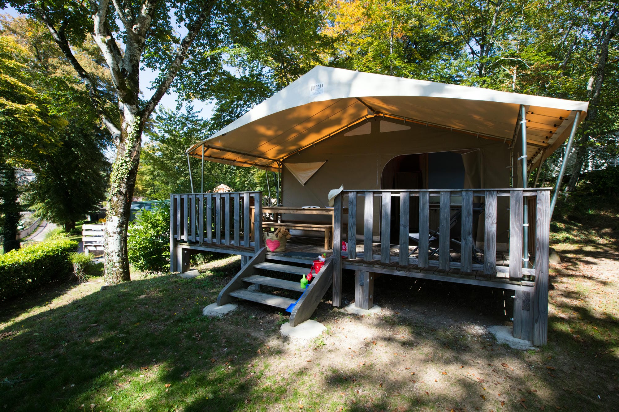 Tente lodge installée sur l'herbe en lisière de forêt, Camping Château le Verdoyer