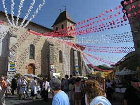 Rue de village animée lors de la Félibrée du Périgord avec ses guirlandes festives et son marché artisanal autour d'une église romane