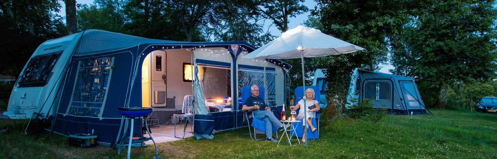 Couple assis devant une tente bleue avec parasol, camping en Périgord au Château le Verdoyer