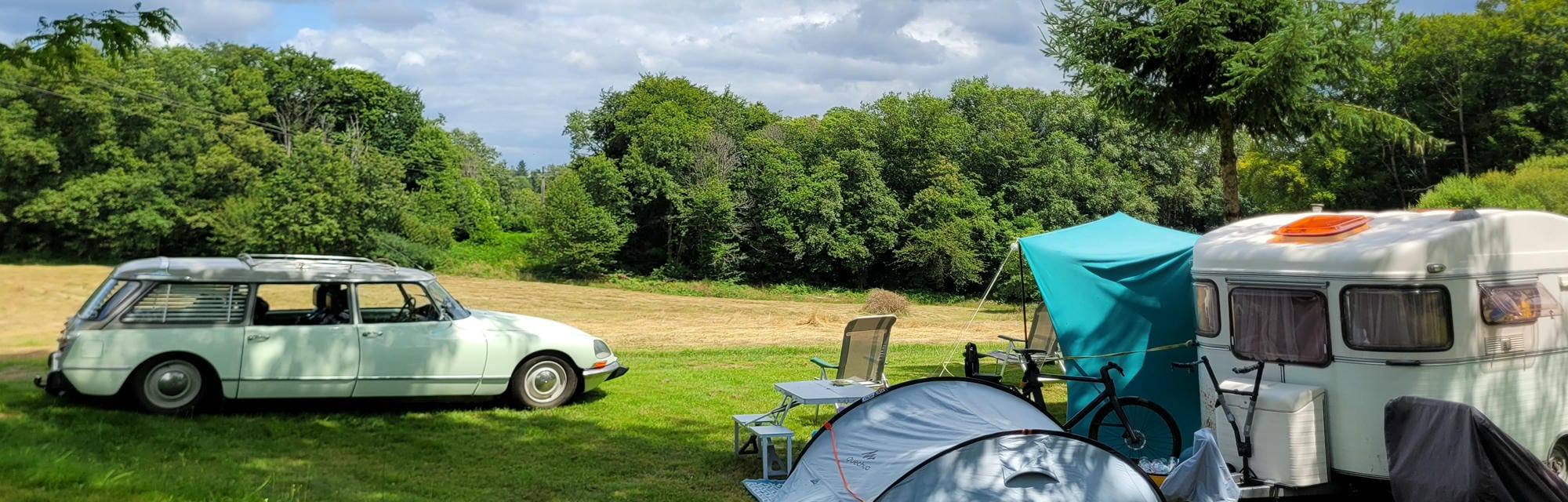 Citroën DS oldtimer et caravane vintage installés sur un emplacement de camping spacieux et verdoyant au Château le Verdoyer