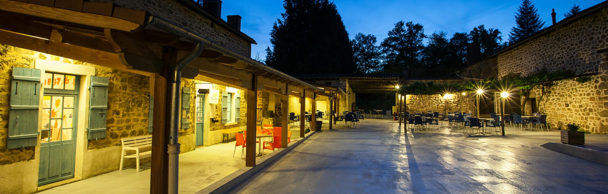 Longue allée centrale du Château le Verdoyer avec tables et chaises, cœur des services du camping