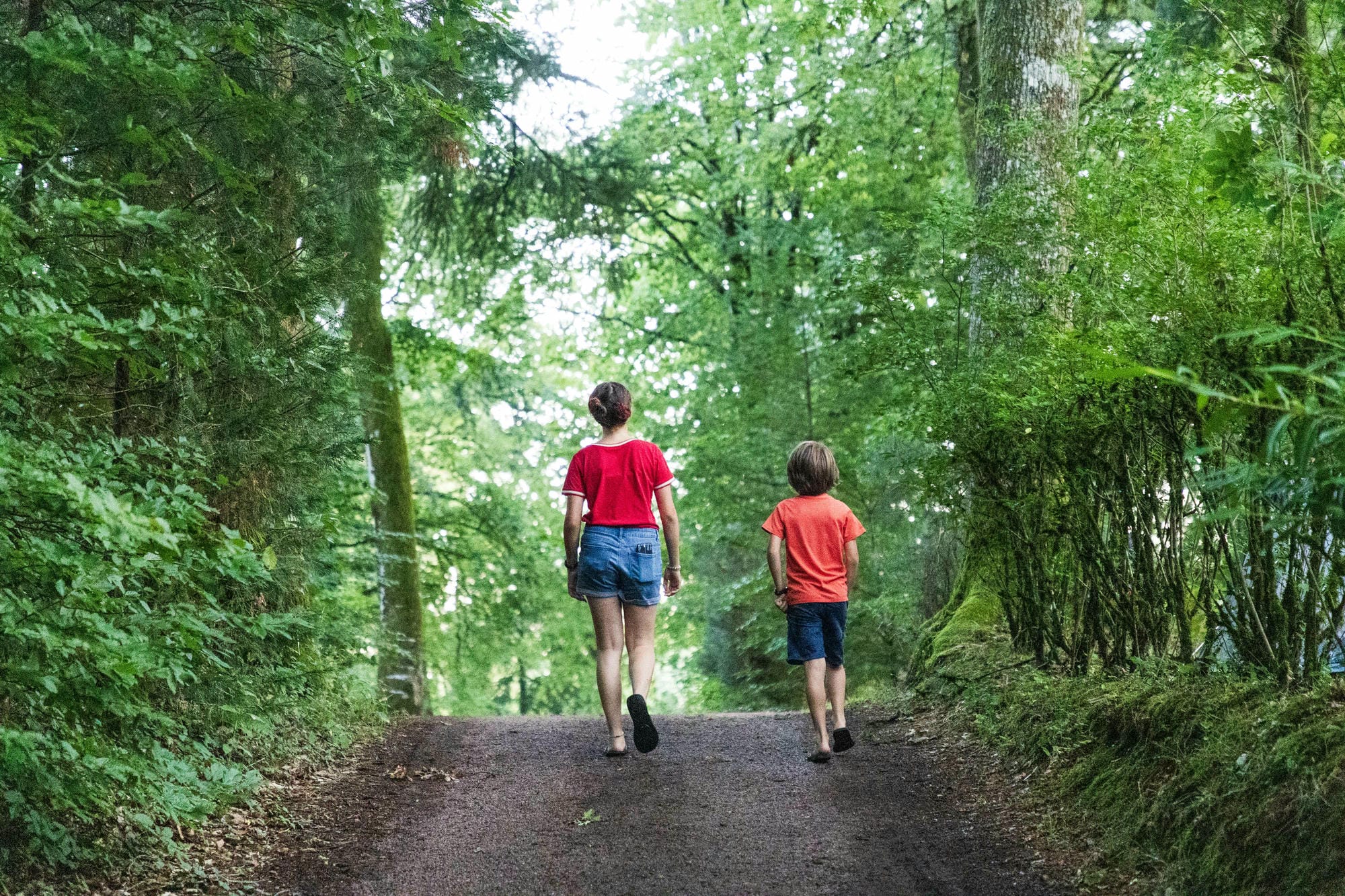 Deux enfants en randonnée pédestre sur un sentier boisé du camping, dans le Périgord Vert