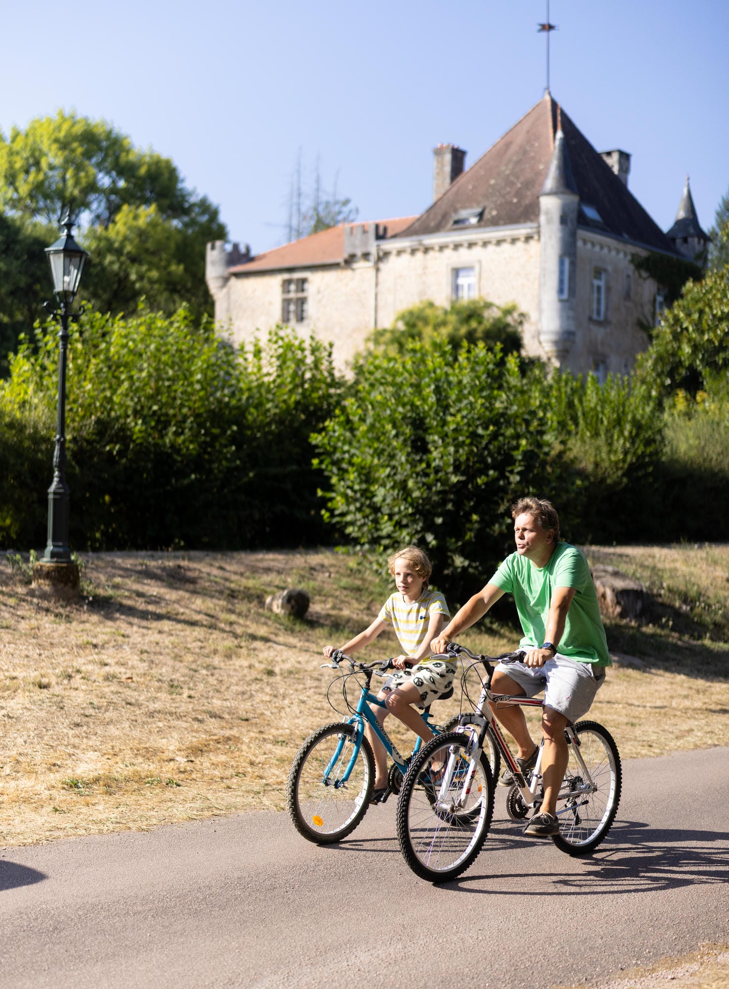 Père et fils en balade à vélo devant le Château le Verdoyer en Dordogne