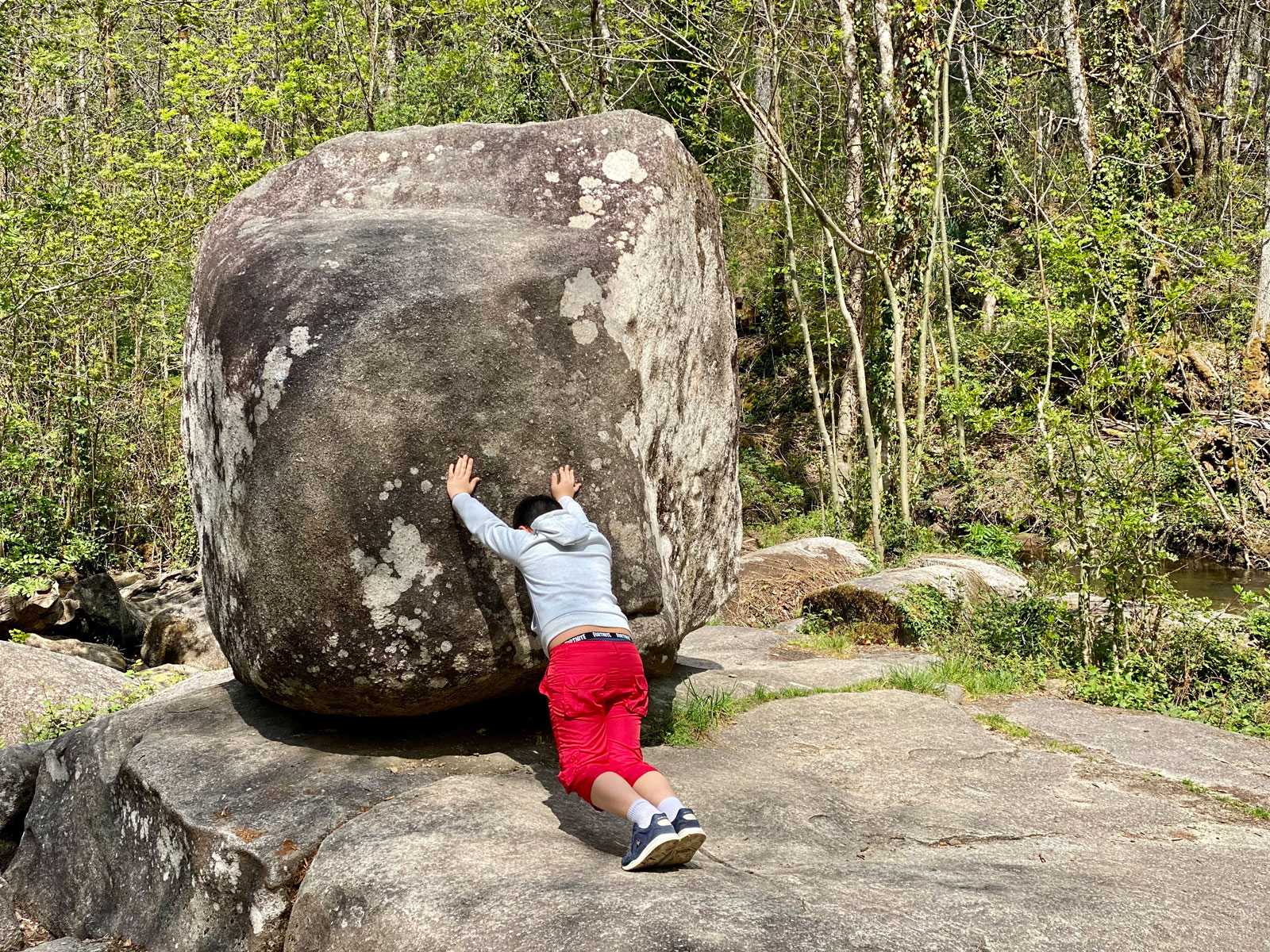 Enfant s'amusant à pousser le Roc Branlant, rocher de granite en Périgord Vert, randonnée et découverte nature autour du Château le Verdoyer