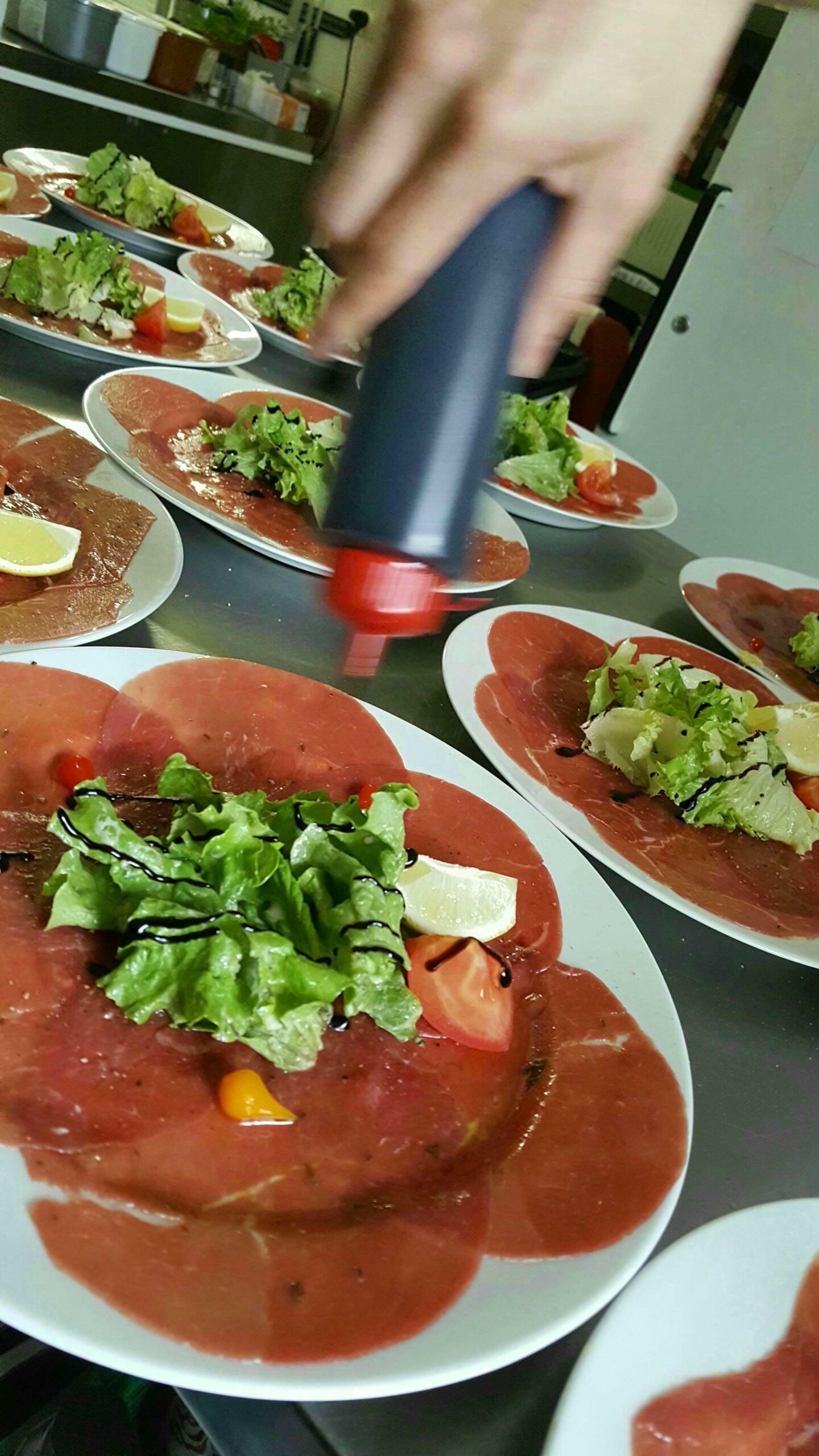 Nombreuses assiettes garnies de Carpaccio de bœuf, chef ajoutant de la sauce, préparation d'un banquet au Verdoyer