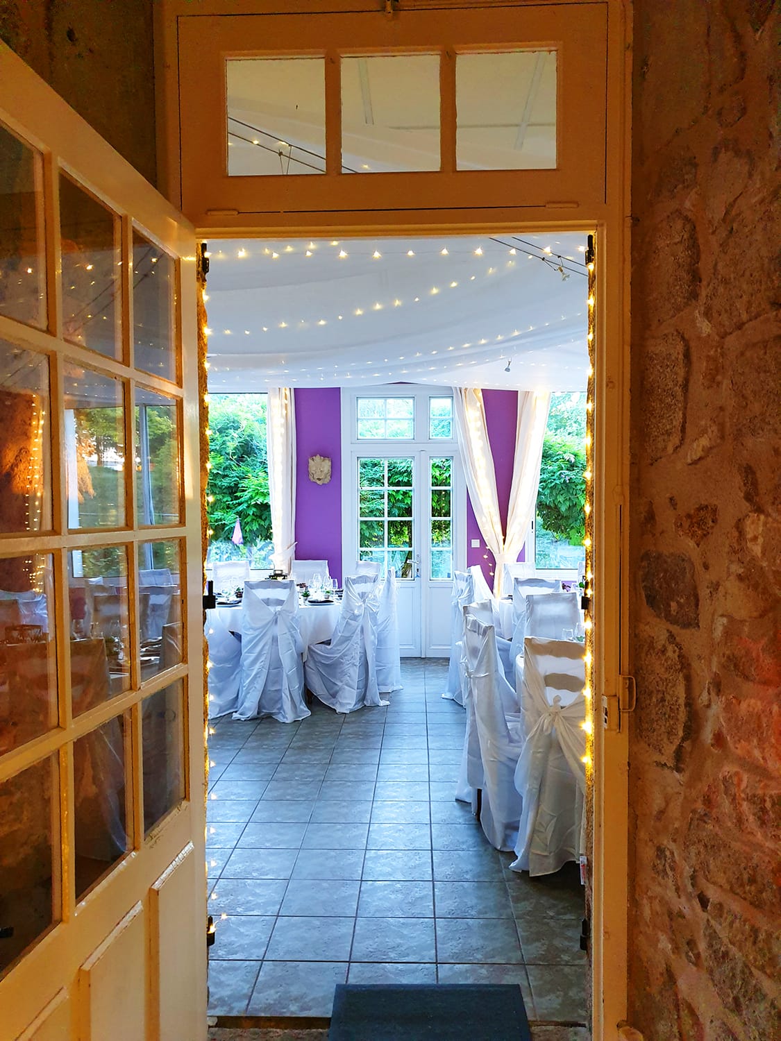 Entrée d'une salle de réception avec tables dressées en blanc pour un mariage au Château le Verdoyer