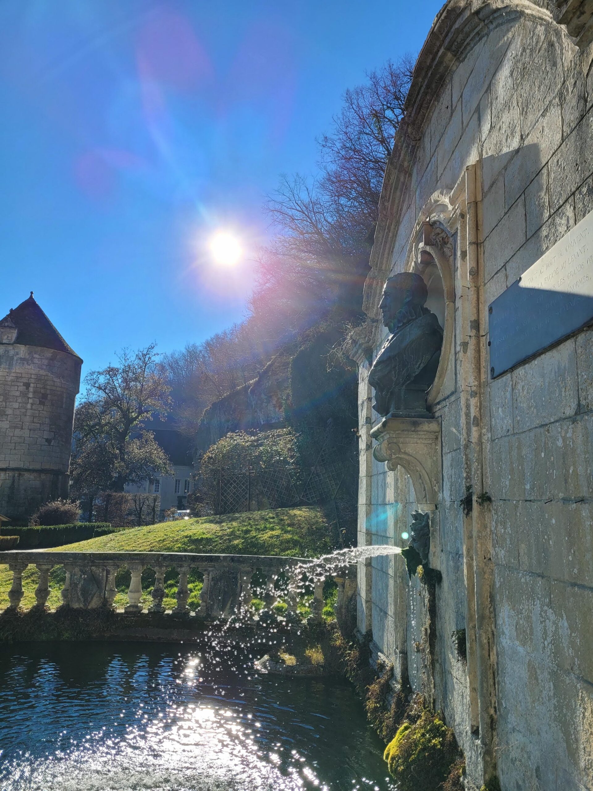 Fontaine avec statue au centre, détail architectural à Brantôme avec le soleil derrière