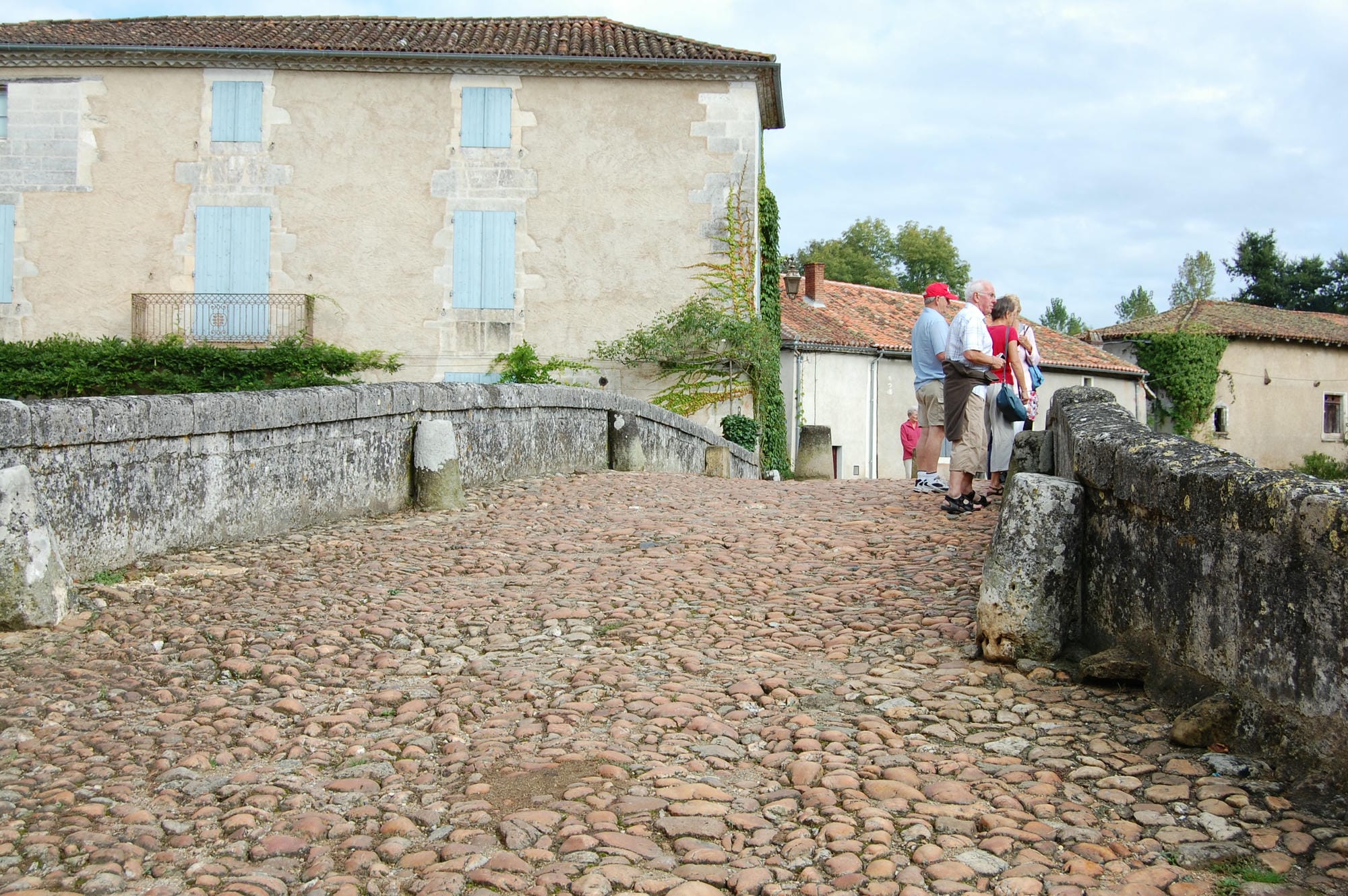 Visiteurs sur le pont en pierre de St-Jean-de-Côle, devant un bâtiment du village