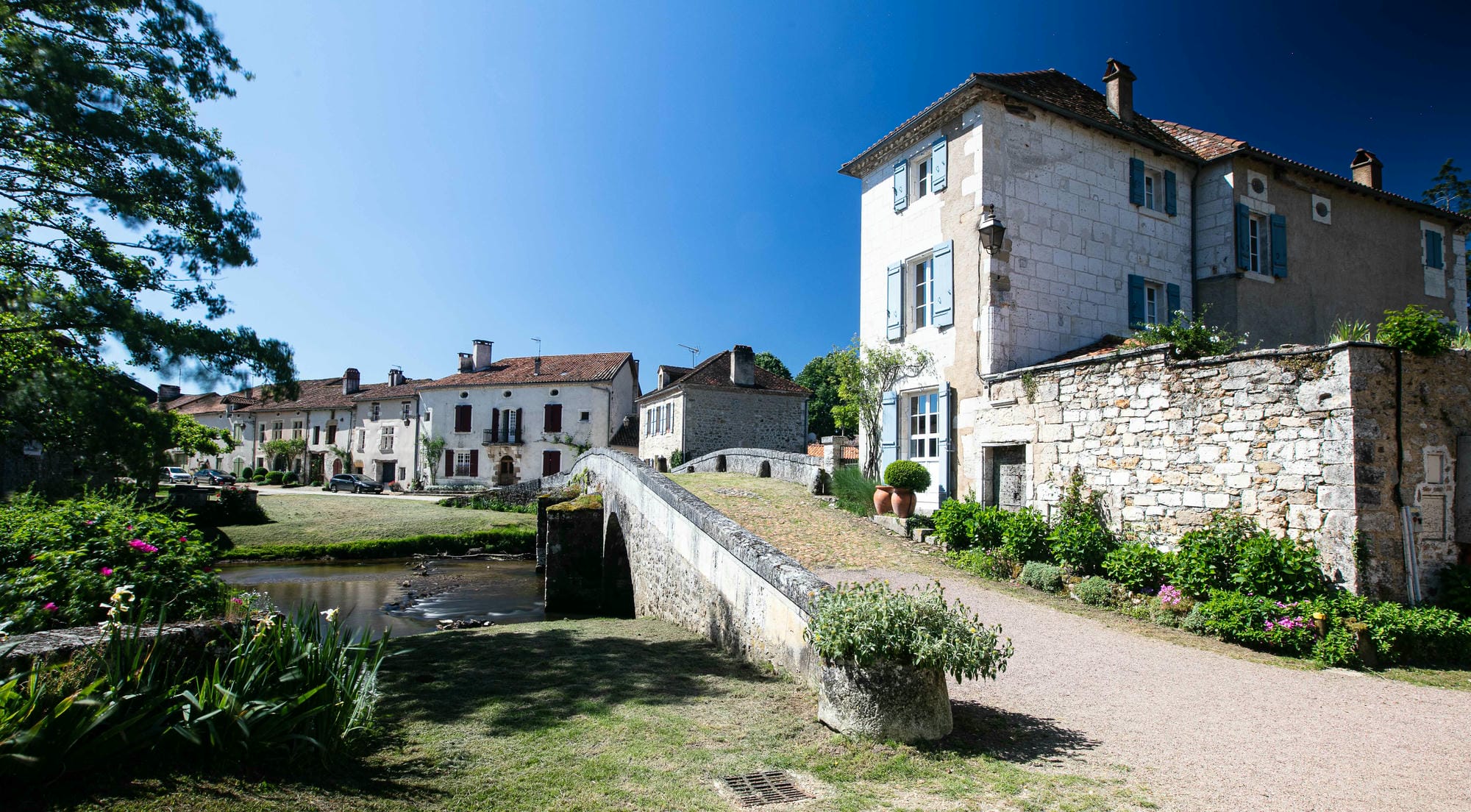 Pont en pierre sur la Côle devant un bâtiment du village de St-Jean-de-Côle