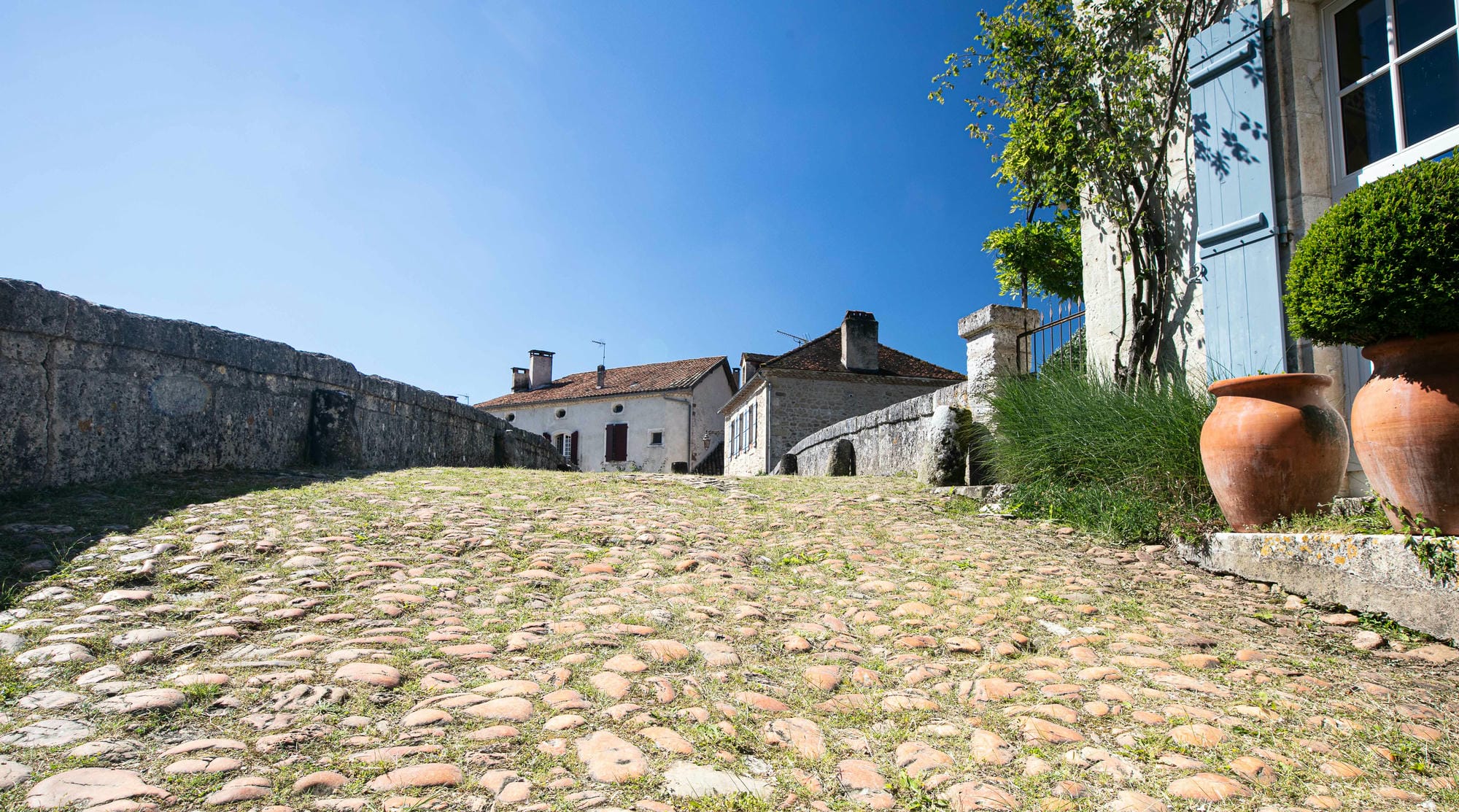 Deux grands vases décoratifs au bord d'une route pavée près du pont de St-Jean-de-Côle