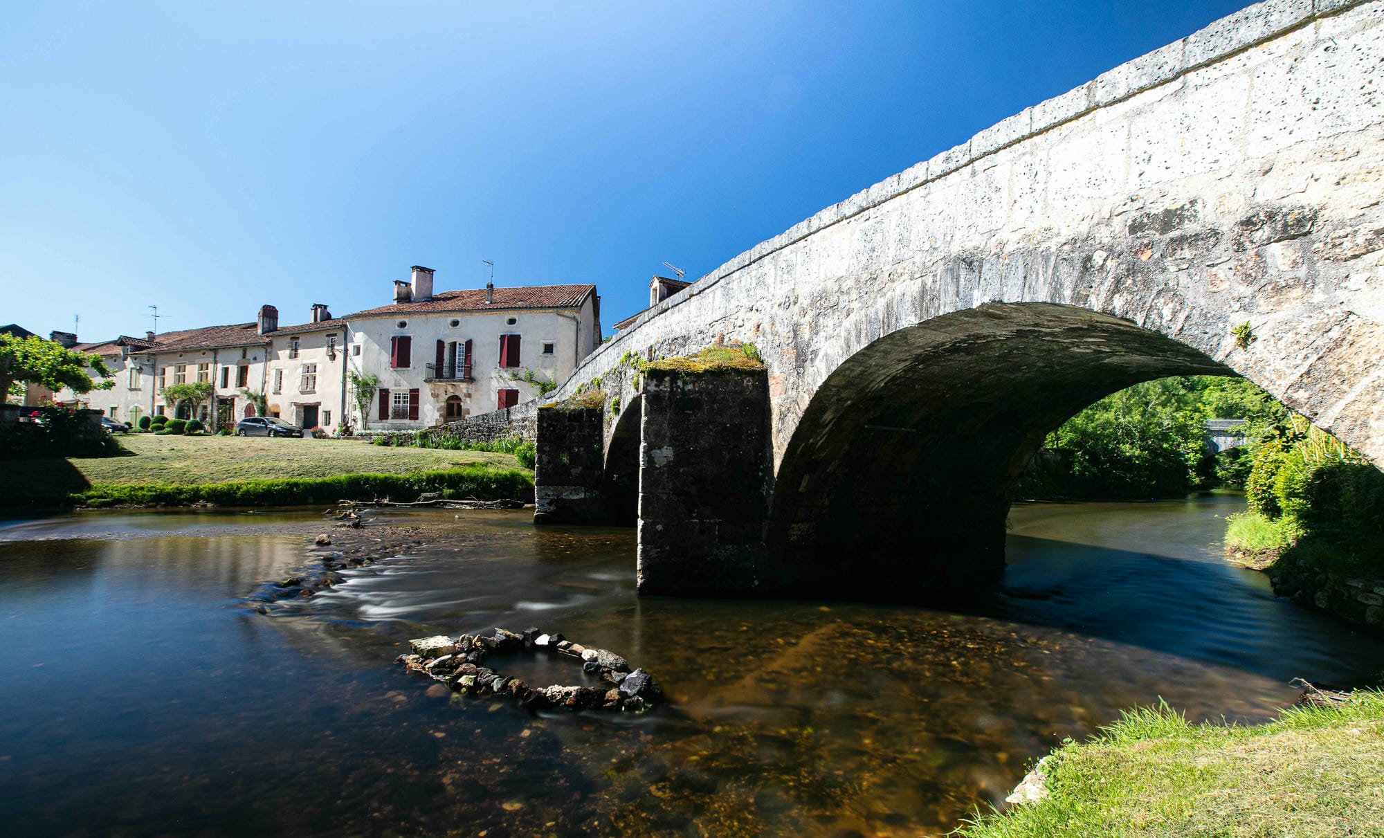 Pont en pierre sur la Côle avec un bâtiment historique en arrière-plan à St-Jean-de-Côle